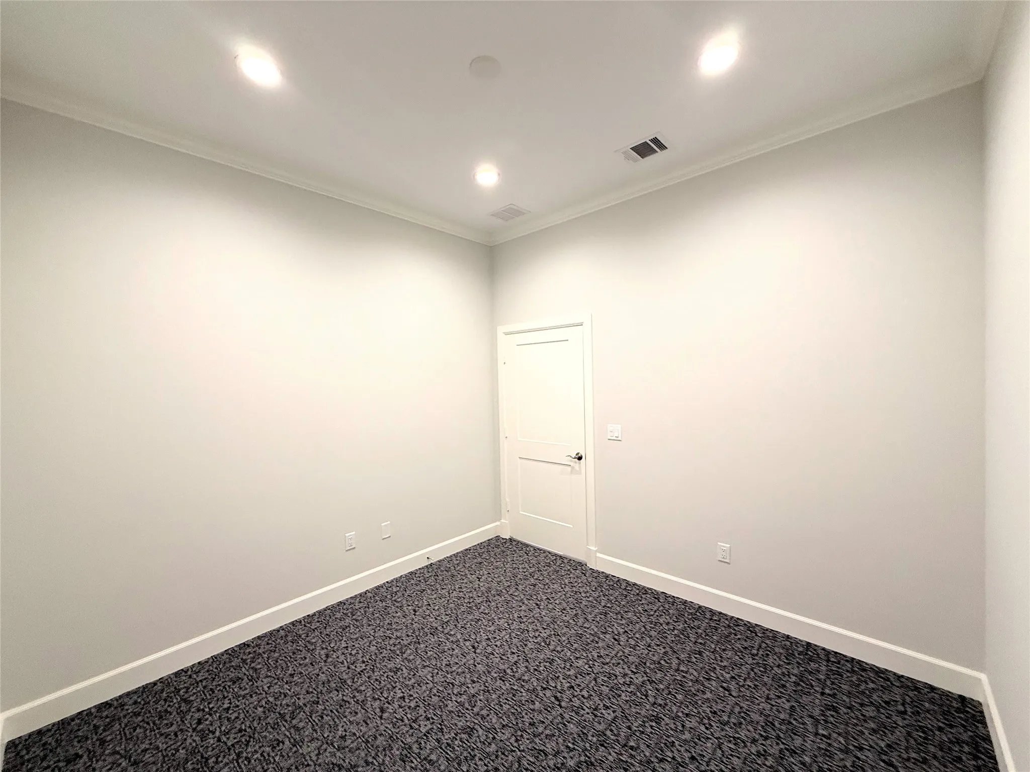 White interior door with black hardware, crown molding, recessed lighting, and patterned carpet flooring