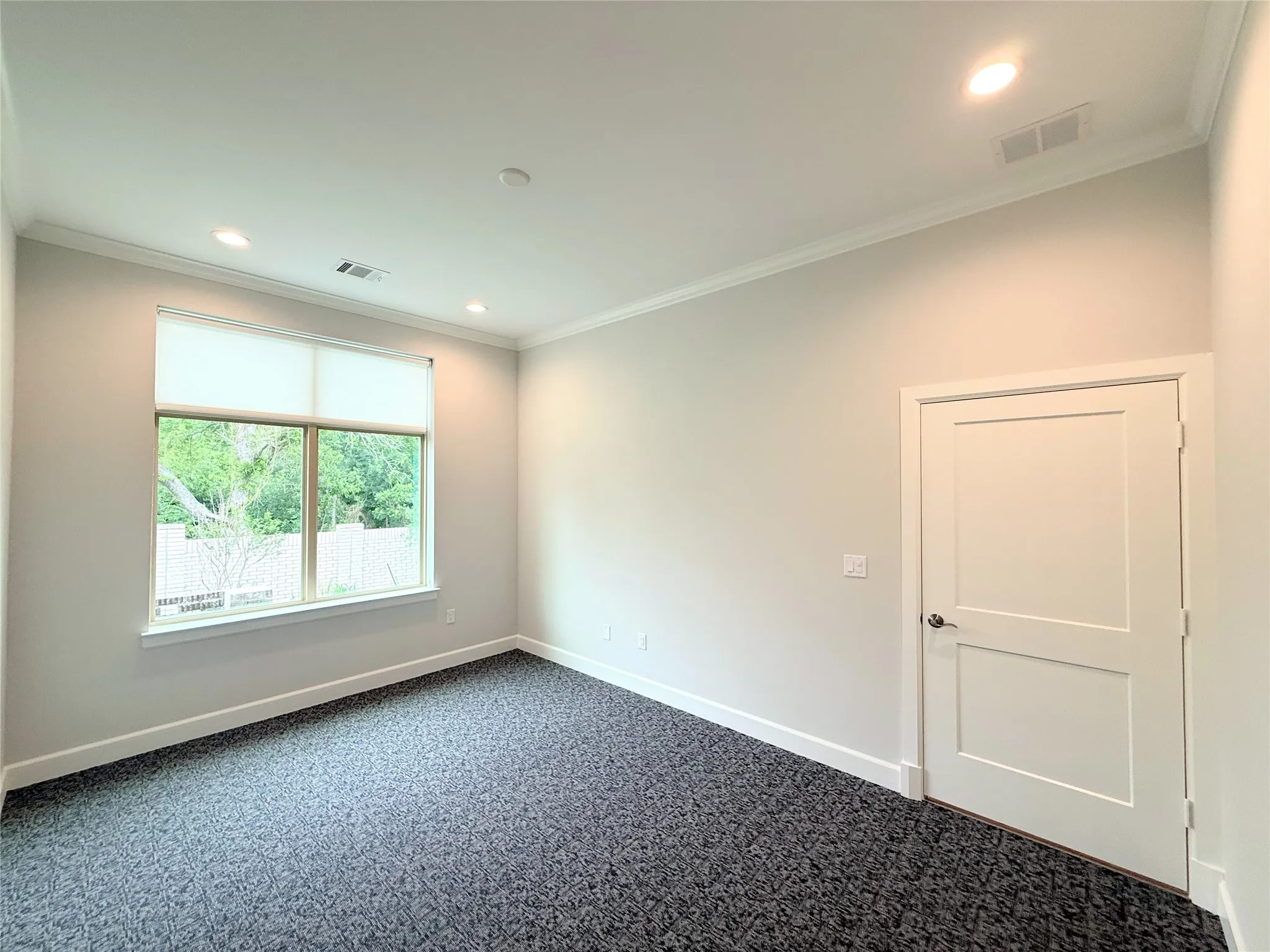 Room with patterned carpeting, a large window with roller shades, and a two-panel interior​​‌​​​​‌​​‌‌​‌‌​​​‌‌​‌​‌​‌​​​‌​​ door