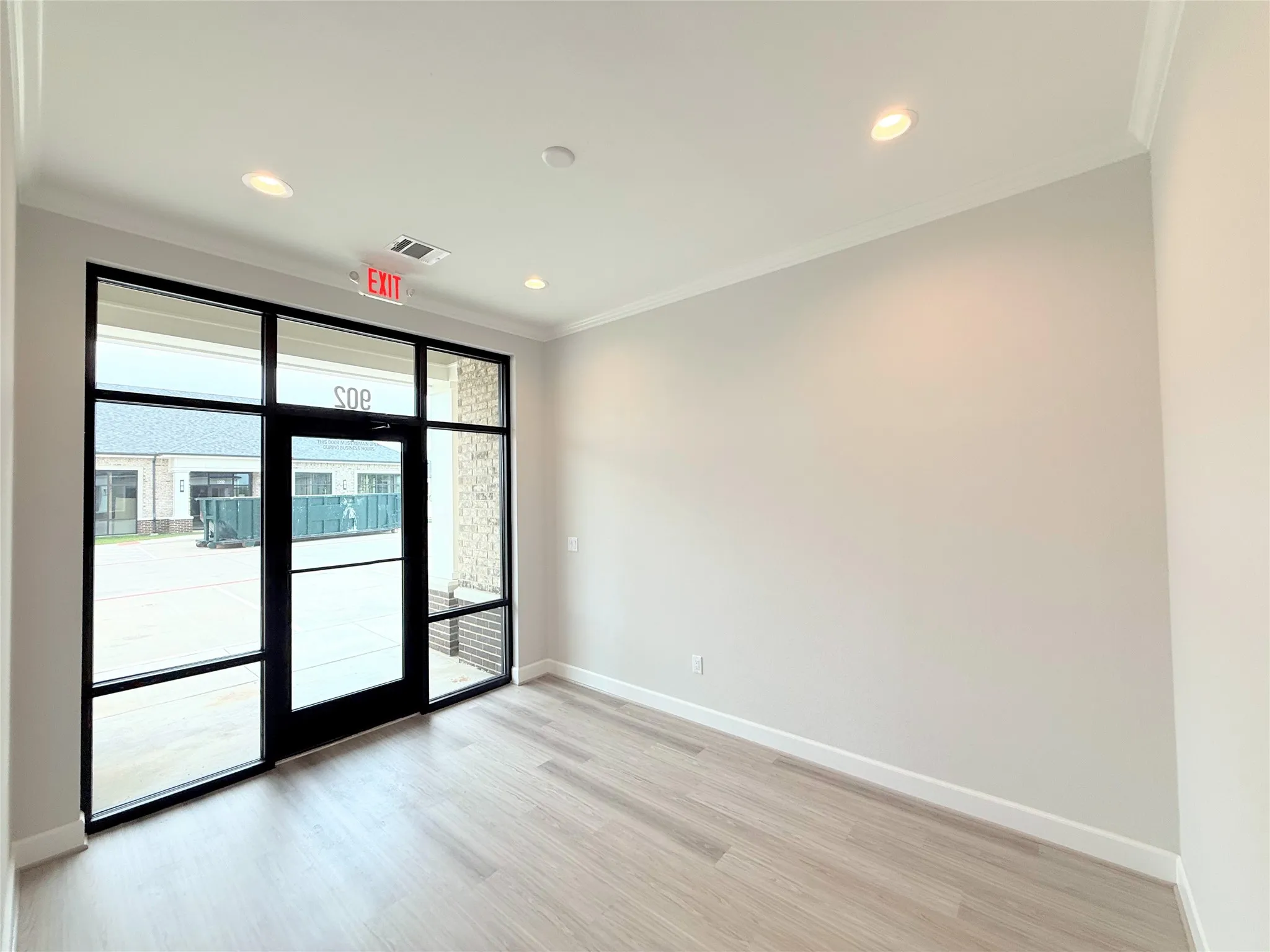 Spacious room with expansive glass storefront, wood-finish flooring, recessed lighting, crown molding, and neutral wall paint