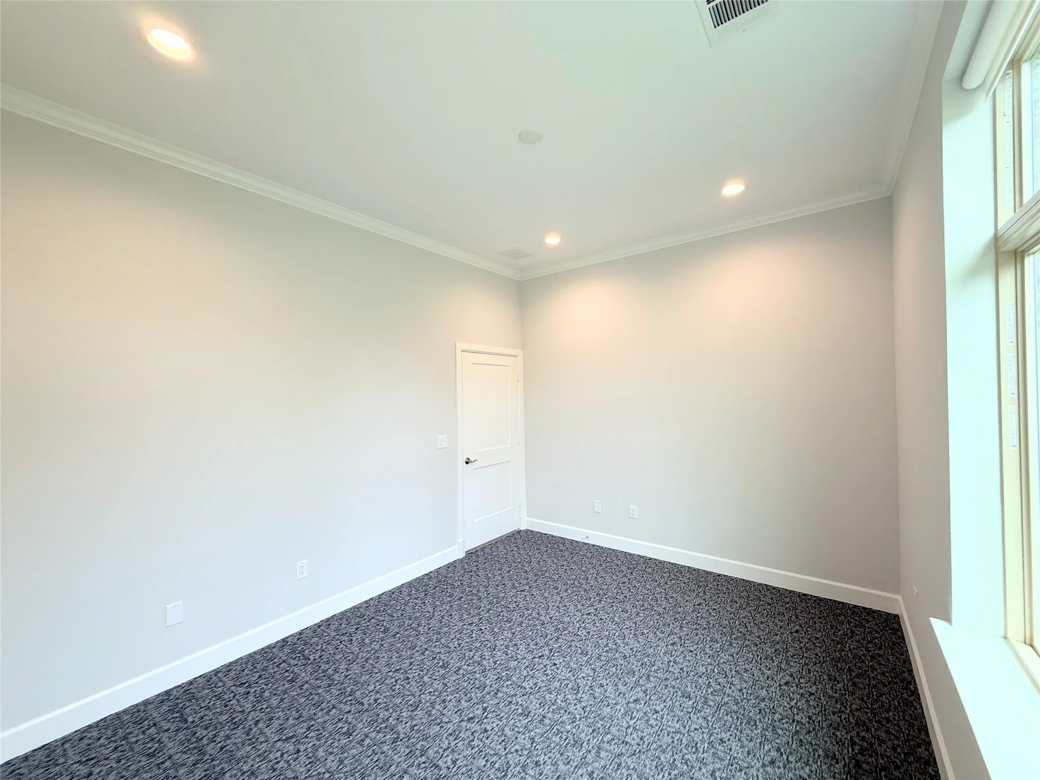 Spacious room featuring neutral painted walls, recessed lighting, crown molding, white baseboards, and patterned carpeting