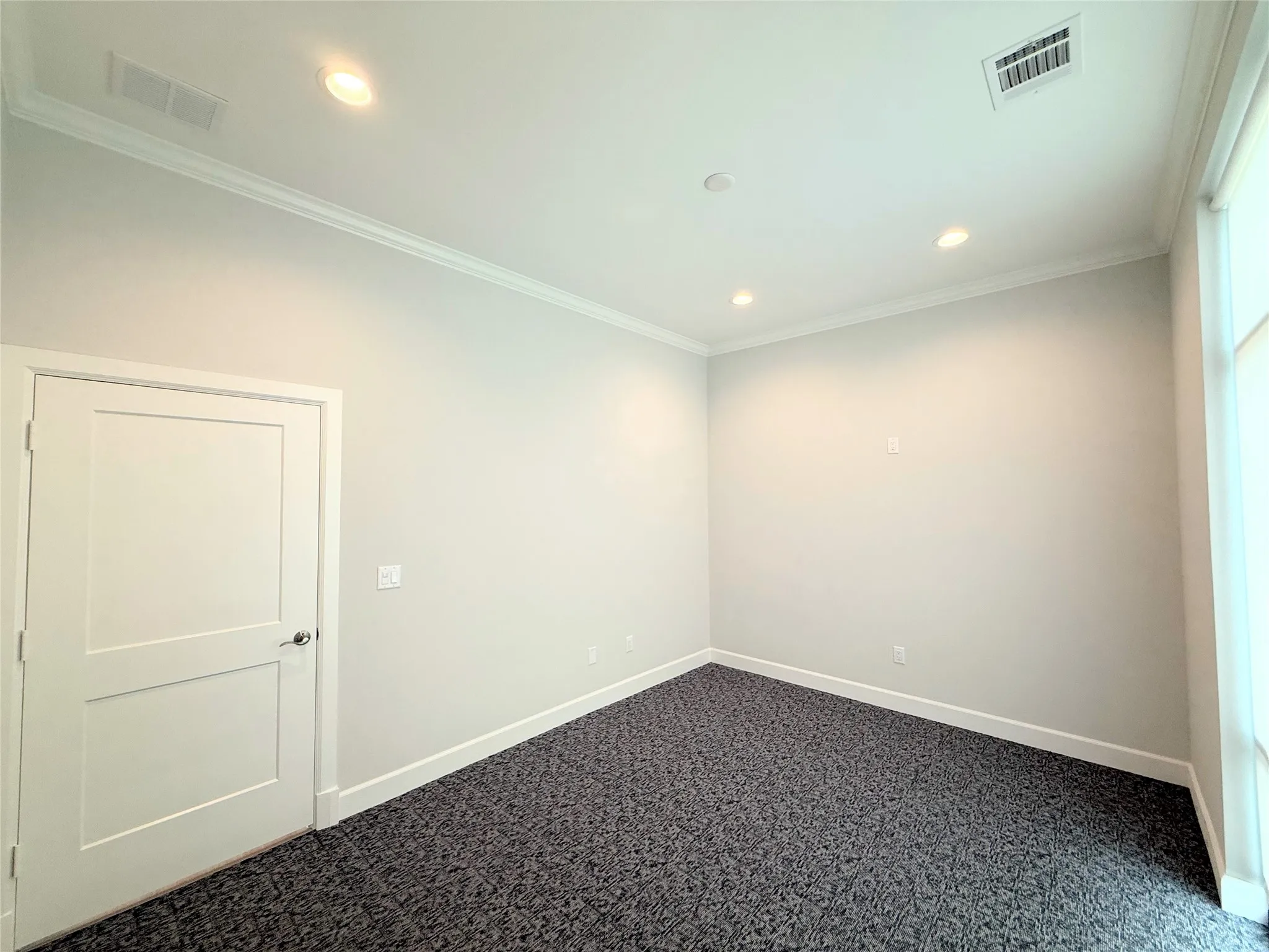 Recessed lighting illuminates this room, featuring light gray walls, dark patterned carpet, and white trim molding