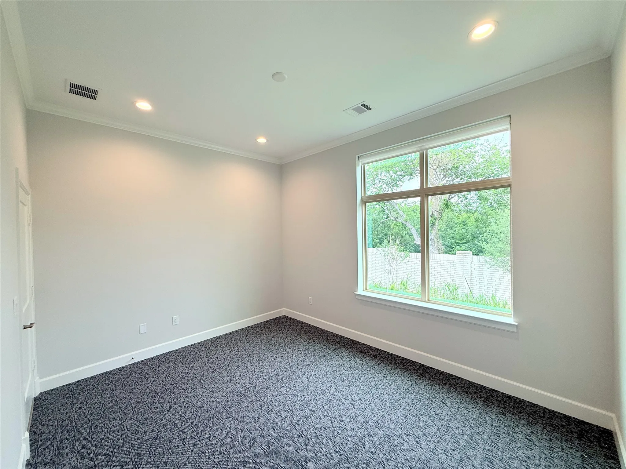 Spacious room featuring a large multi-pane window, recessed lighting, crown molding, a white paneled door with a silver handle, and patterned dark gray carpeting