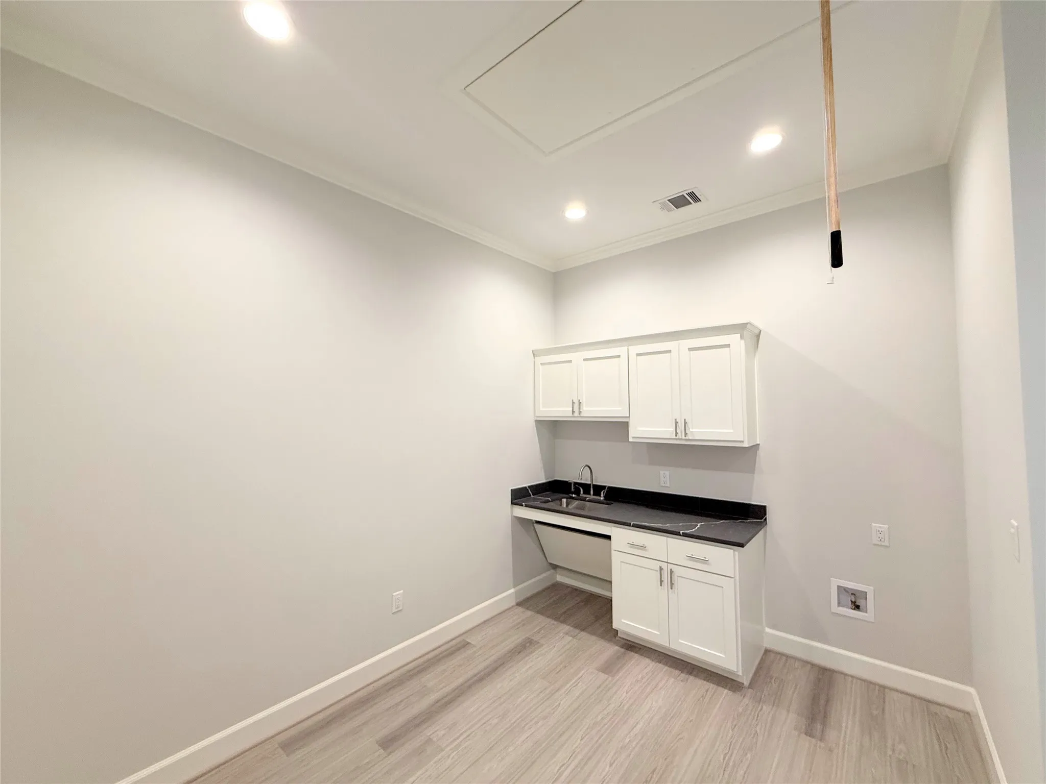 Utility area featuring white shaker-style cabinetry, a dark countertop, and a stainless steel sink with a gooseneck faucet