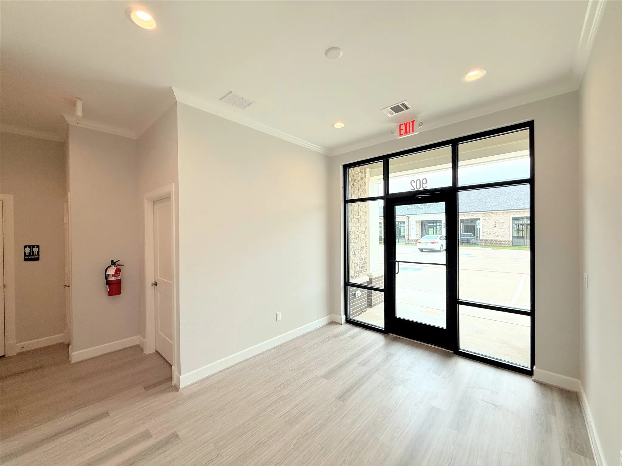 Modern commercial entry featuring a full-glass door with black framing, wood-finish flooring, recessed lighting, and crown molding