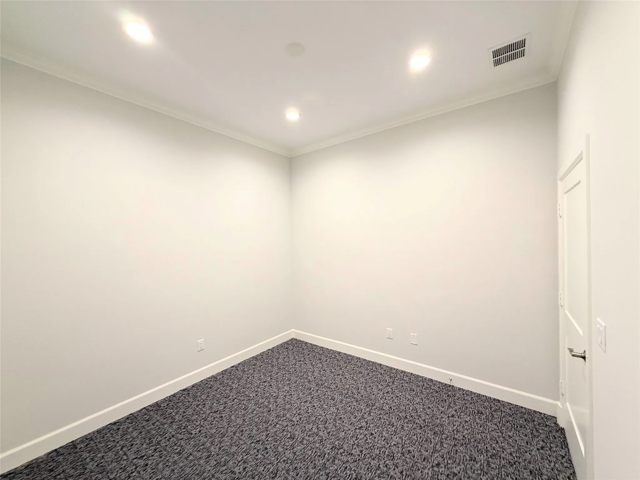 Carpeted room featuring recessed lighting, crown molding, white baseboards, and a paneled interior door with a dark handle