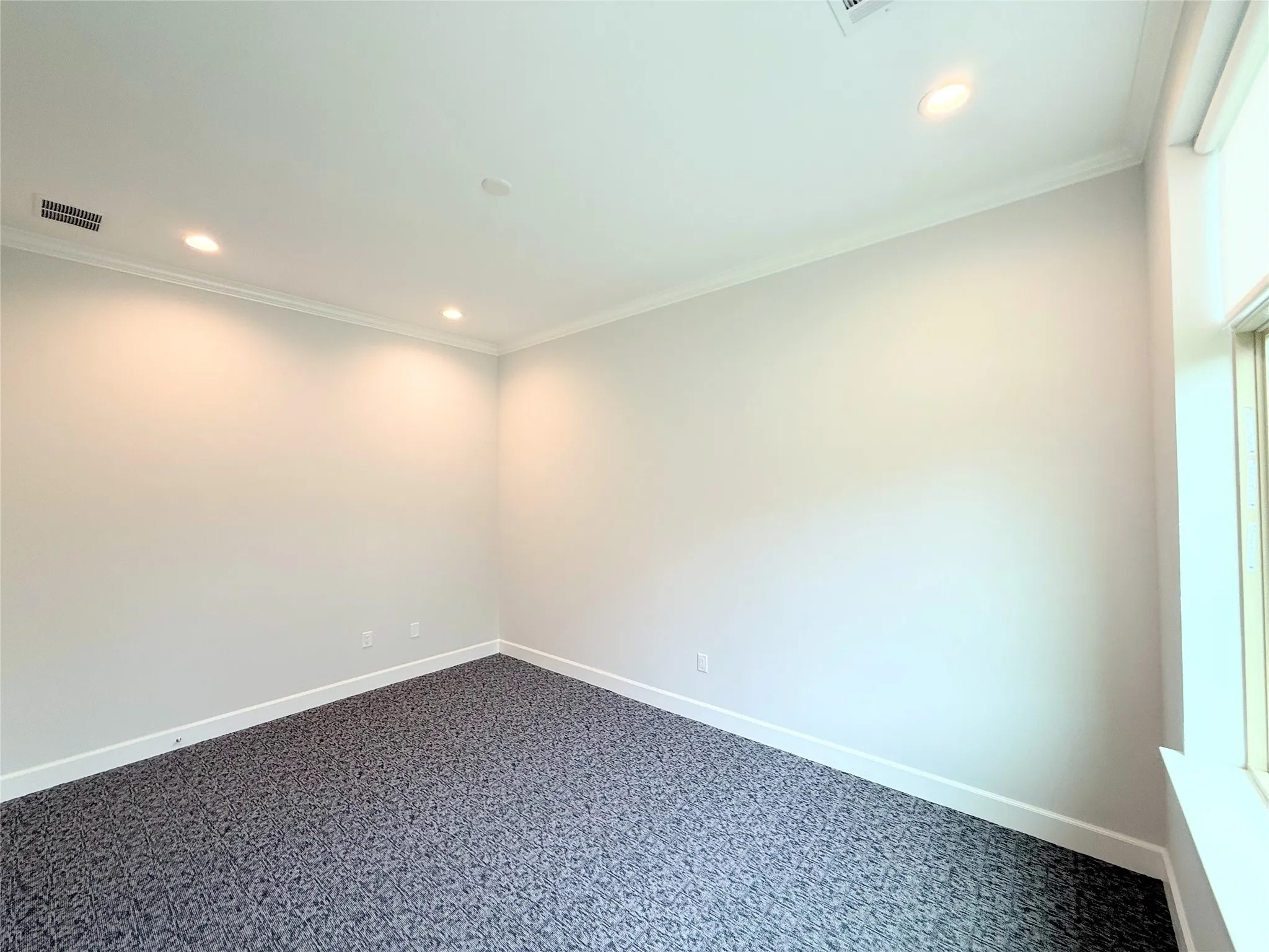Spacious room featuring neutral painted walls, recessed lighting, crown molding, and contrasting baseboards