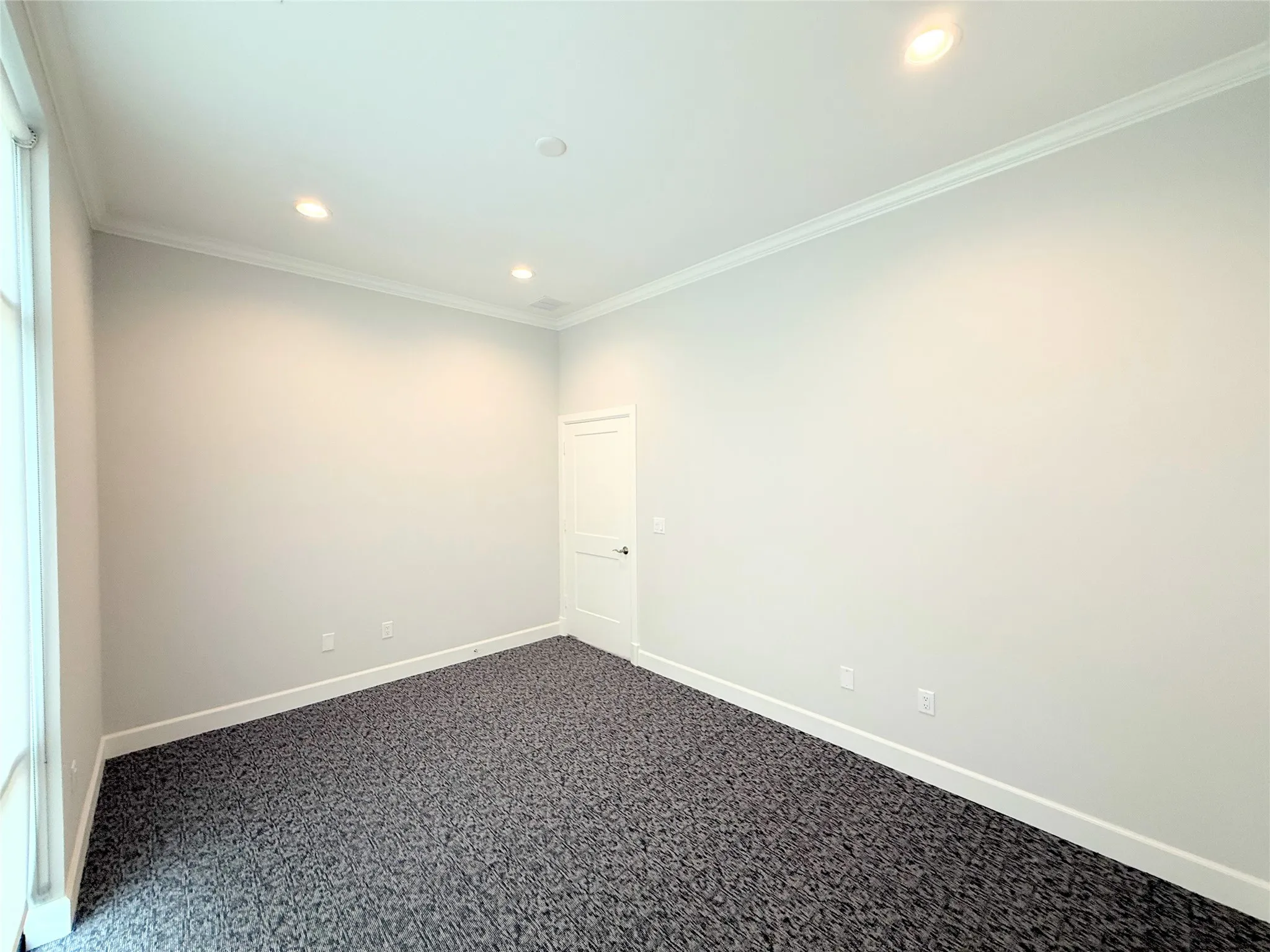 Spacious room featuring patterned carpet flooring, recessed lighting, crown molding, white baseboards, and a white interior door with dark hardware