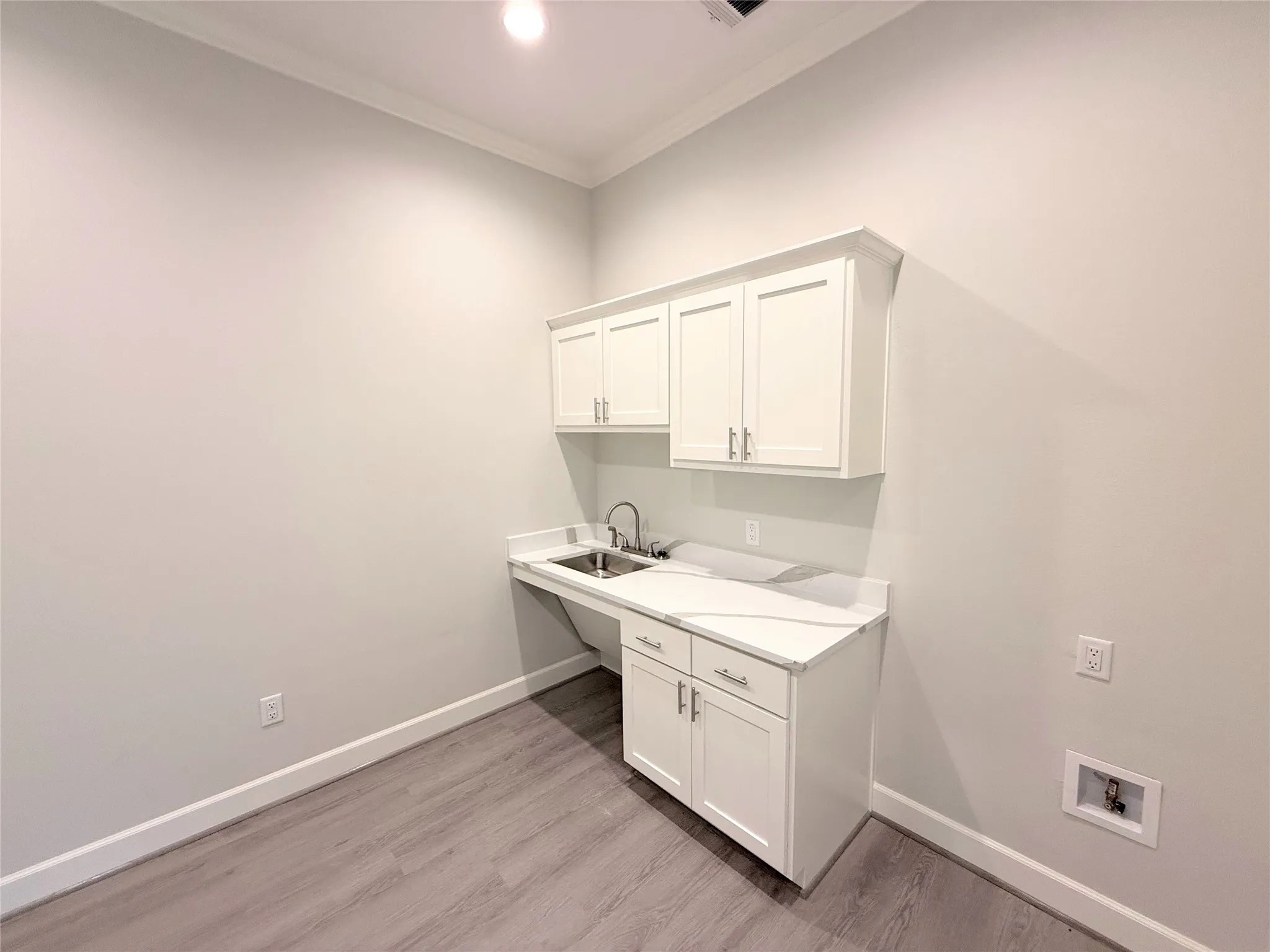 Utility room featuring a built-in sink, white cabinetry, a light-toned countertop, and wood-finish flooring
