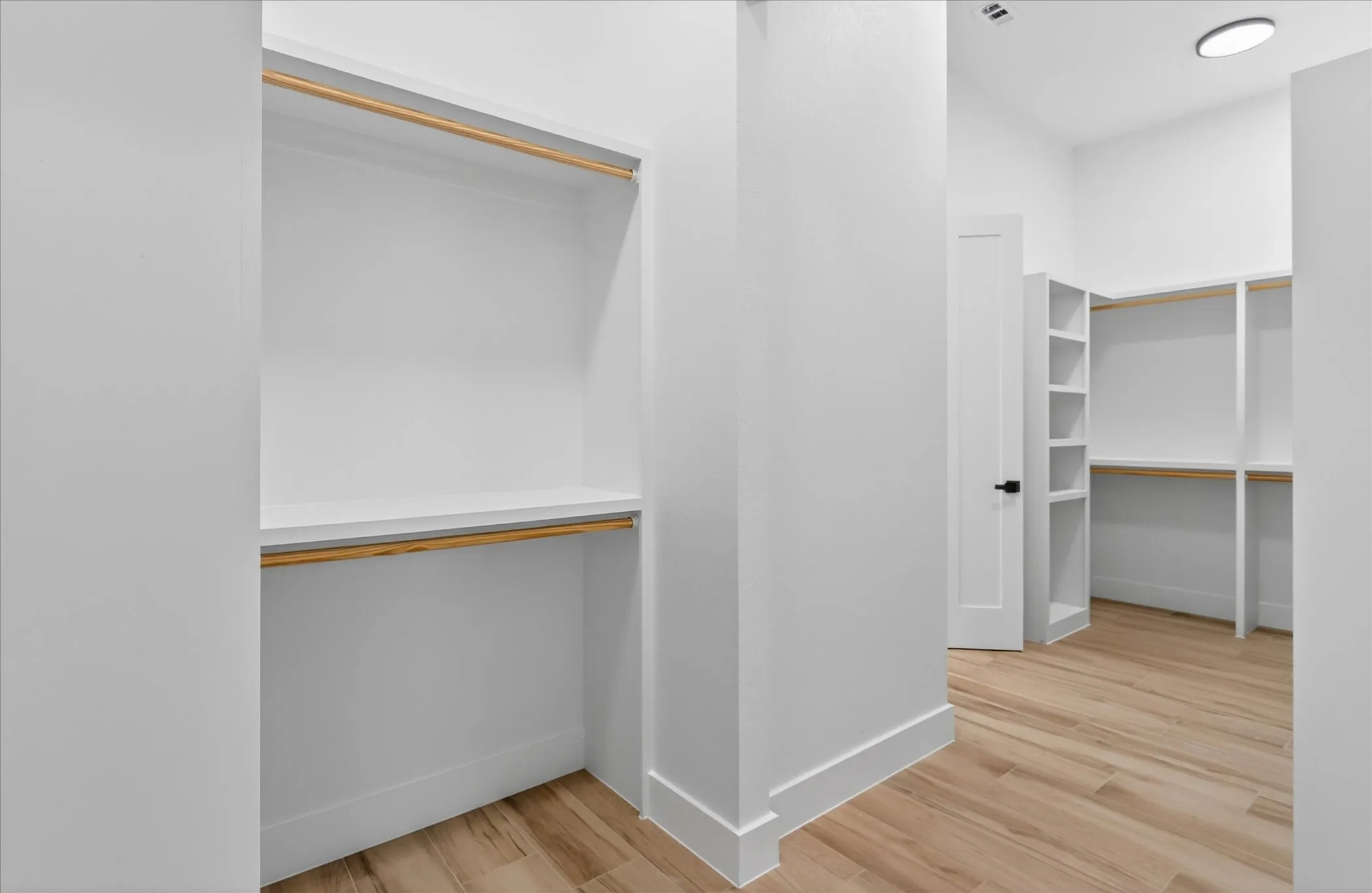 Spacious closet featuring built-in shelving, hanging rods, light wood-finish flooring, and white trim