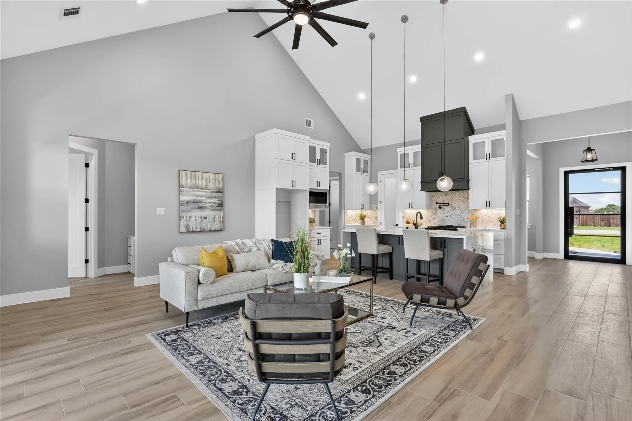 Open-concept living area featuring vaulted ceilings, wood-finish flooring, recessed lighting, a ceiling fan, and a kitchen with an island, pendant lights, and a range hood