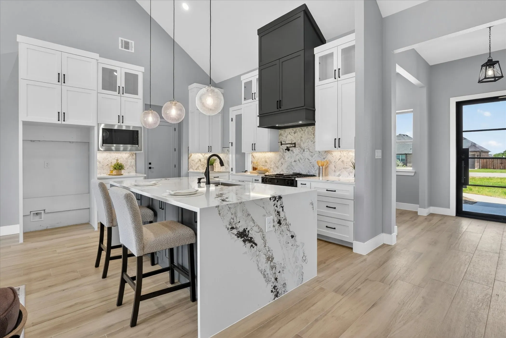 Contemporary kitchen featuring an oversized waterfall island with seating, a distinctive black vent hood, stainless steel appliances, and wood-finish flooring