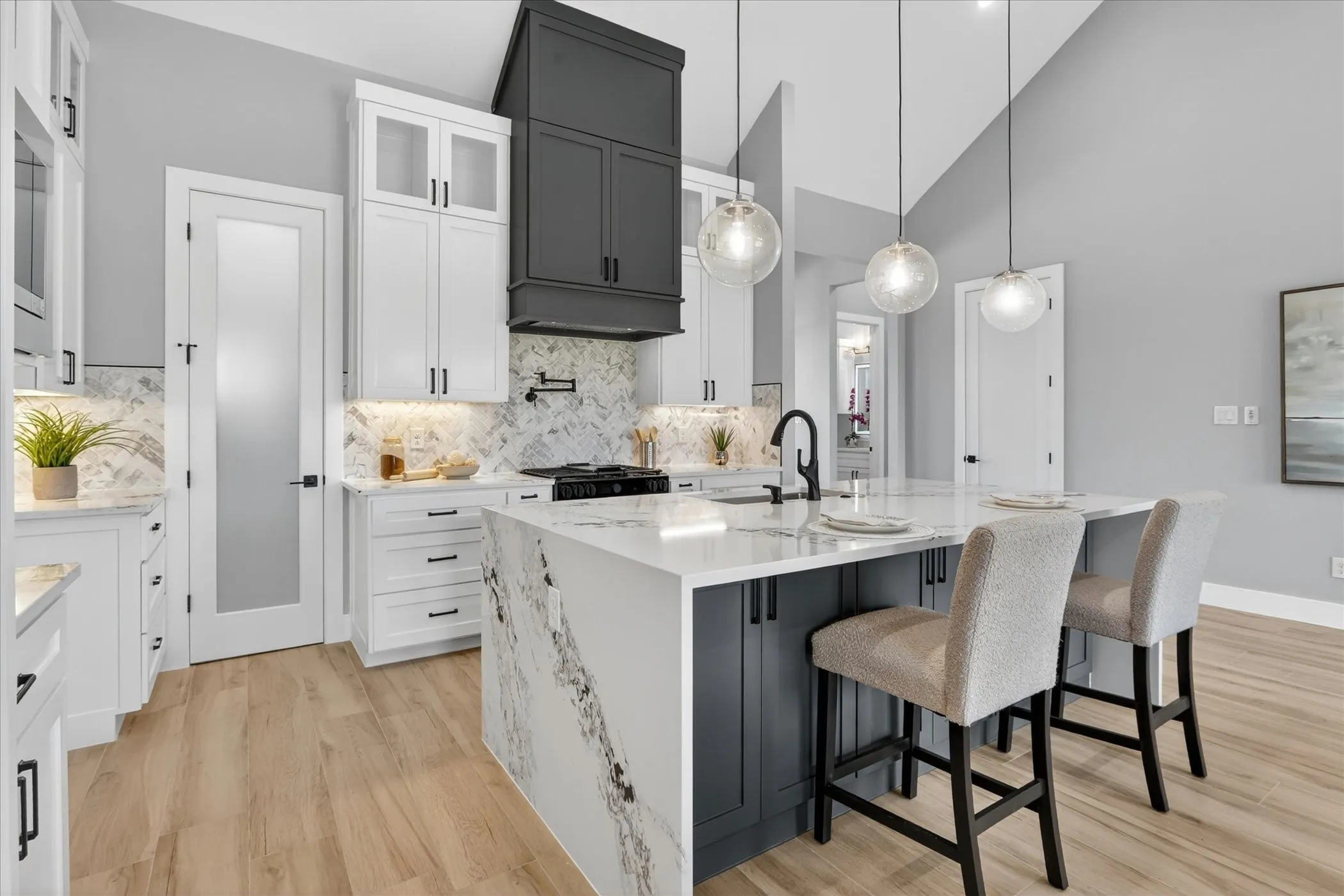 Kitchen featuring a waterfall-edge island with seating, a gas range with a pot filler, a two-tone cabinetry scheme, and recessed under-cabinet lighting