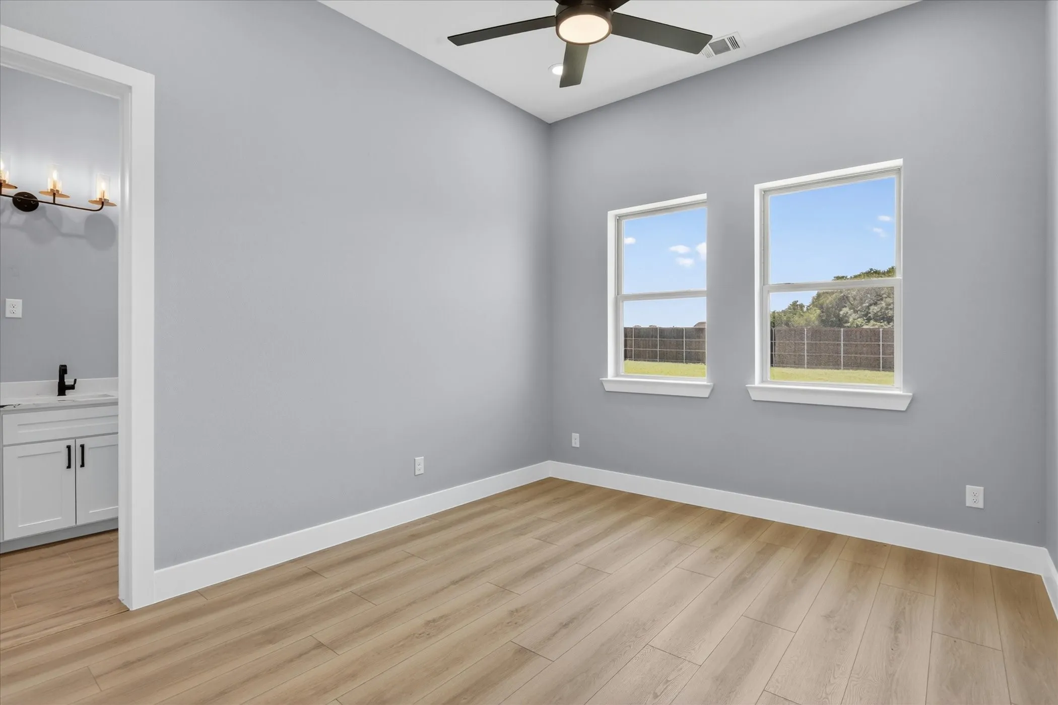 Spacious room featuring wood-finish flooring, light grey walls, and two large windows