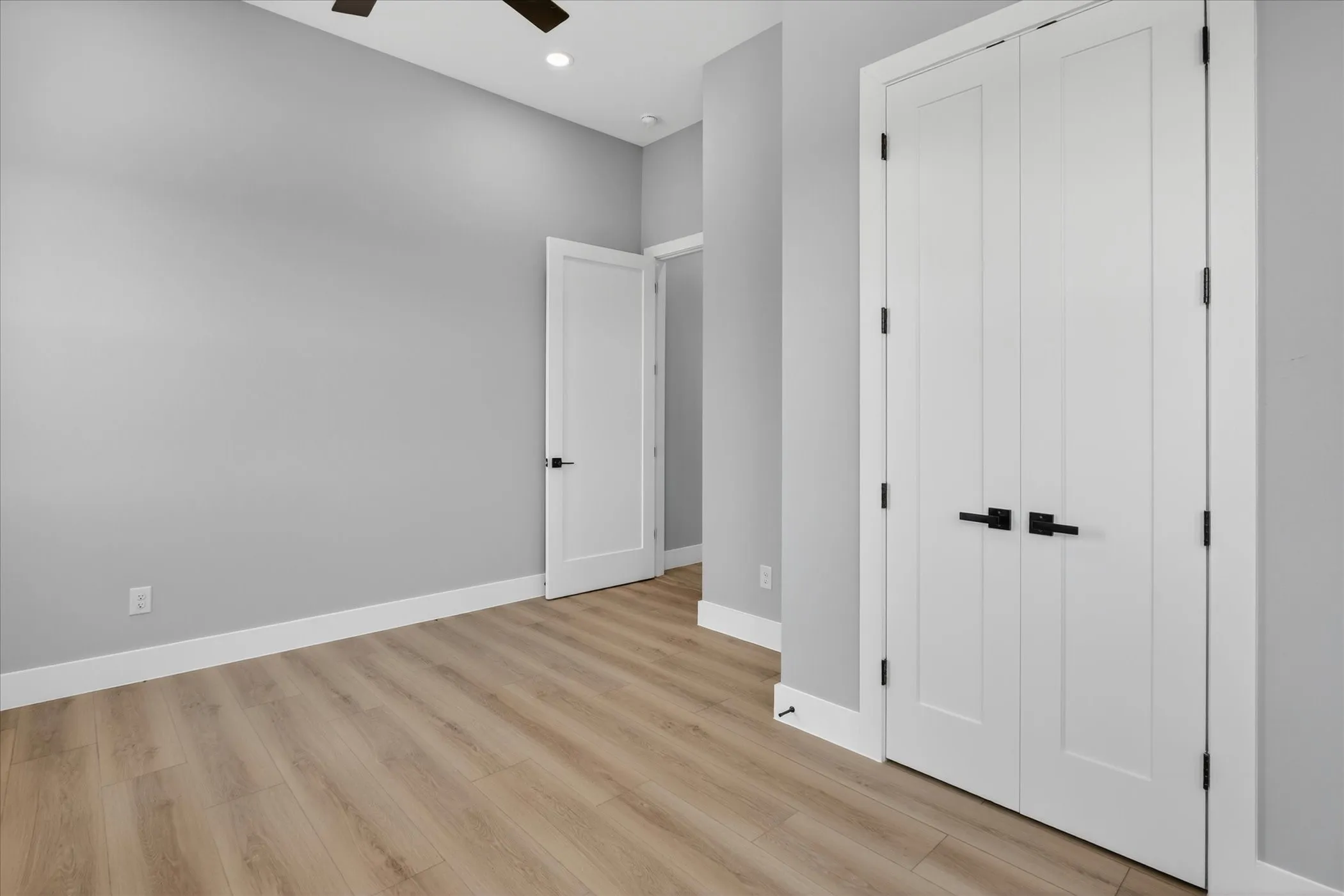 Room featuring light gray walls, wood-finish flooring, white baseboards, and a ceiling fan