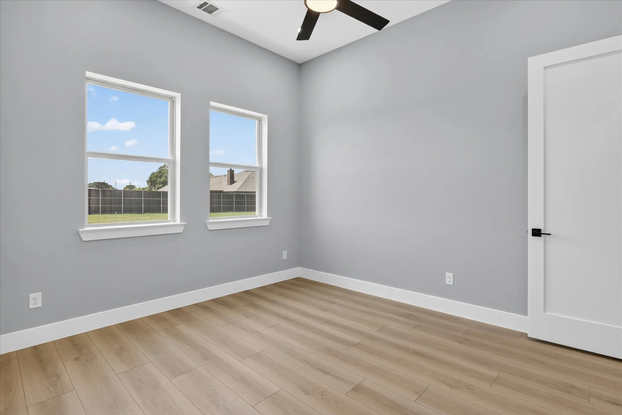 Room featuring wood-finish flooring, two large windows, a ceiling fan, light gray wall paint, and white trim