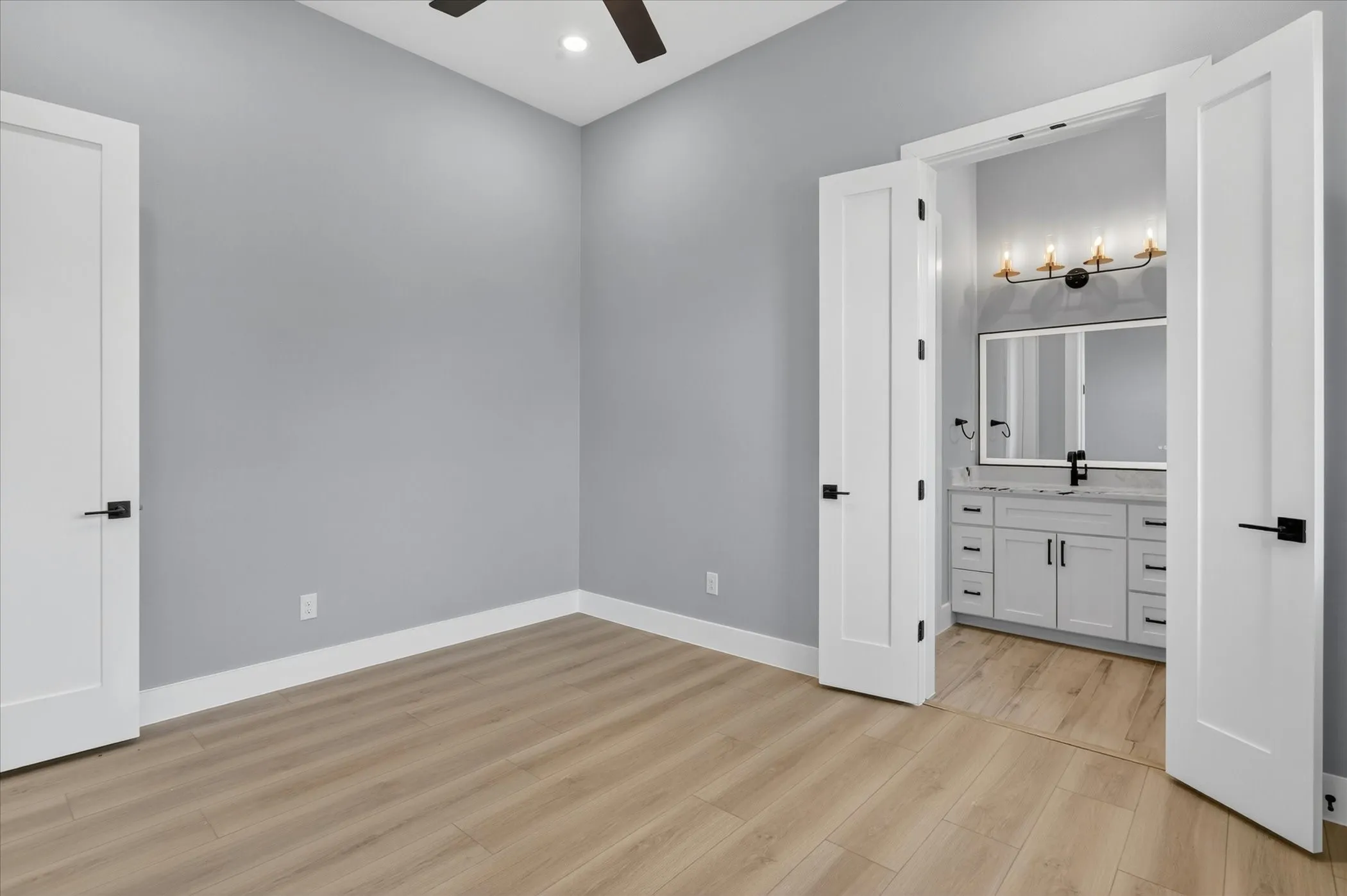 Light wood-finish flooring extending into a bathroom with a white vanity featuring multiple drawers and cabinet storage