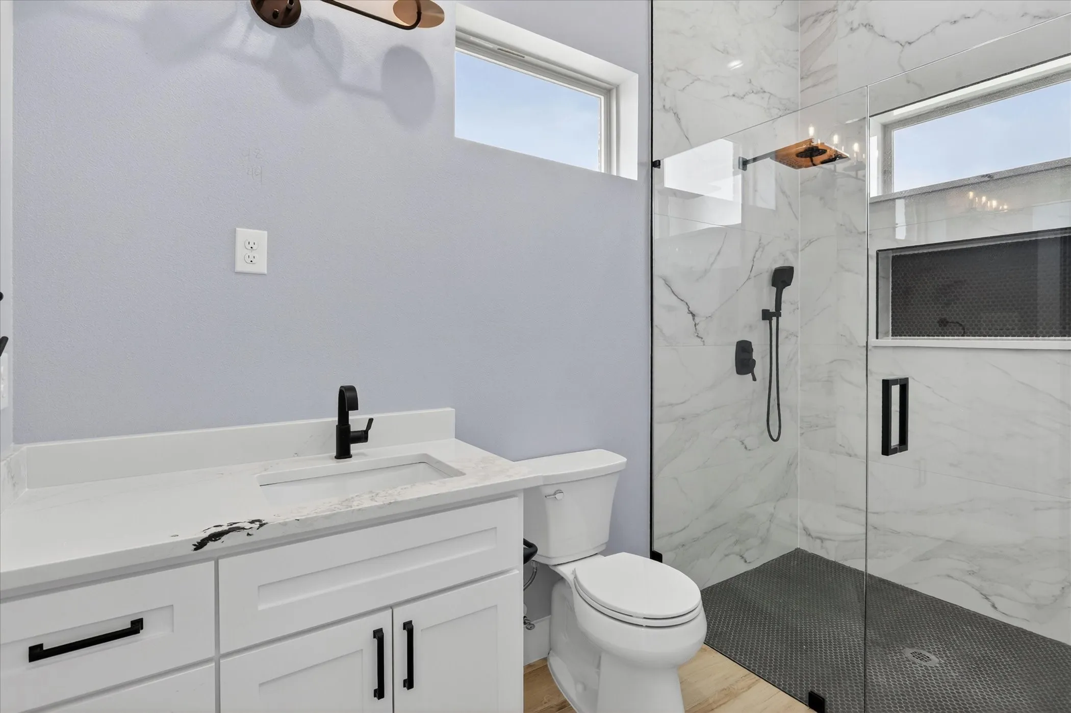Bathroom featuring a glass-enclosed shower with black penny tile flooring and white marble-look wall tiling