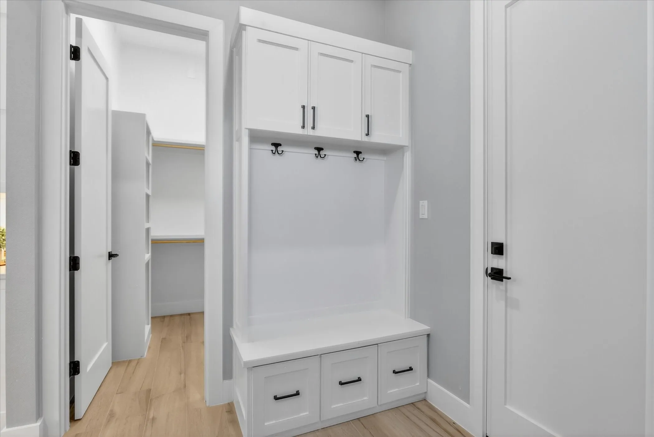 Built-in mudroom cabinetry featuring upper storage, coat hooks, and bench seating with drawers