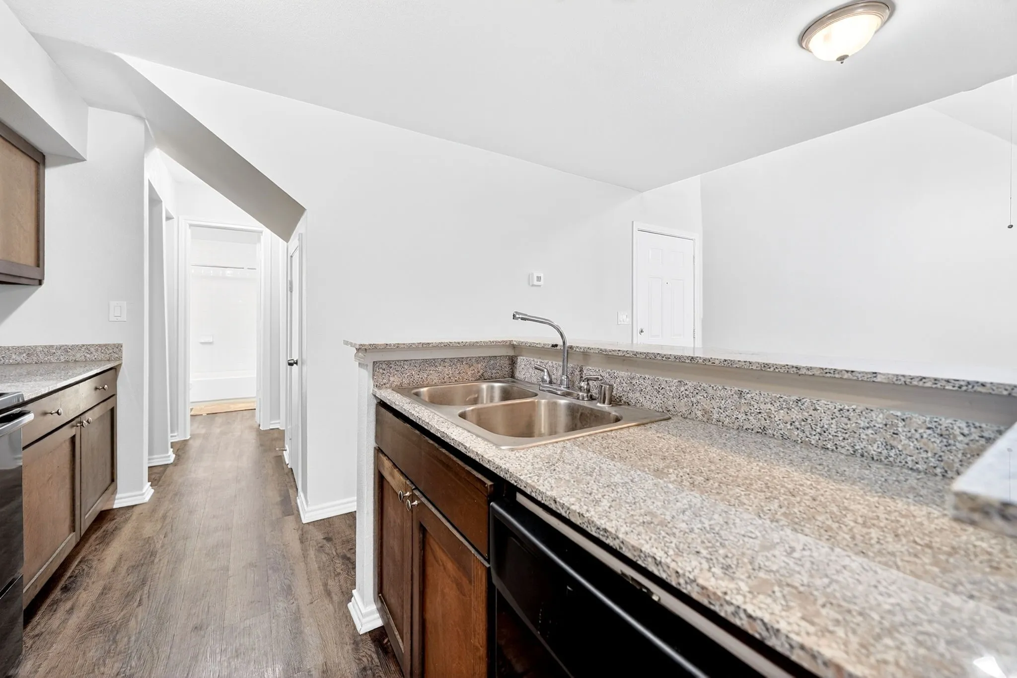 Kitchen featuring a double basin stainless steel sink, granite-style countertops, dark wood-finish cabinetry, and wood-finish flooring