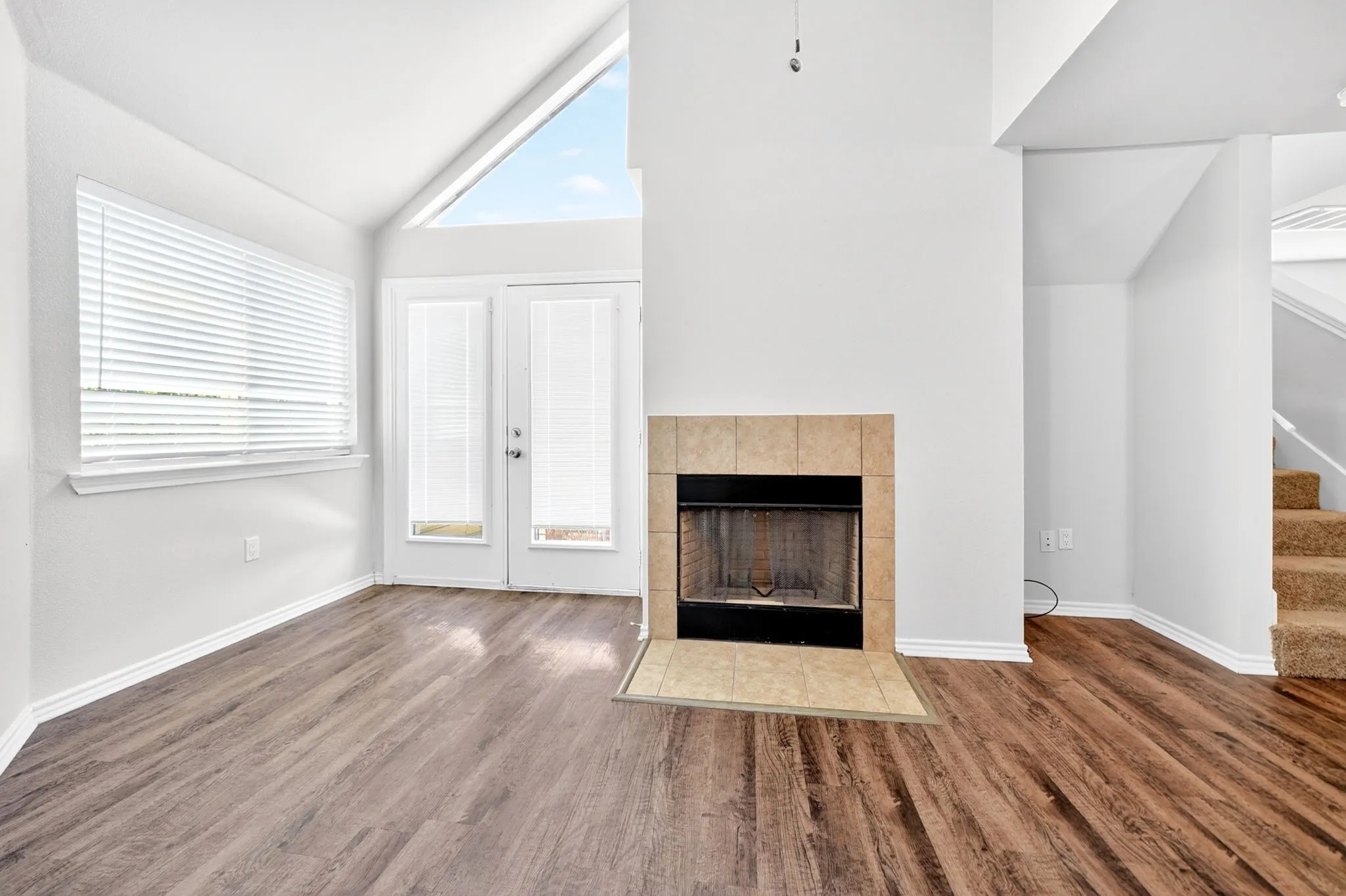 Living space featuring wood-finish flooring, a fireplace with a tile surround and hearth, and a vaulted ceiling with an upper transom window