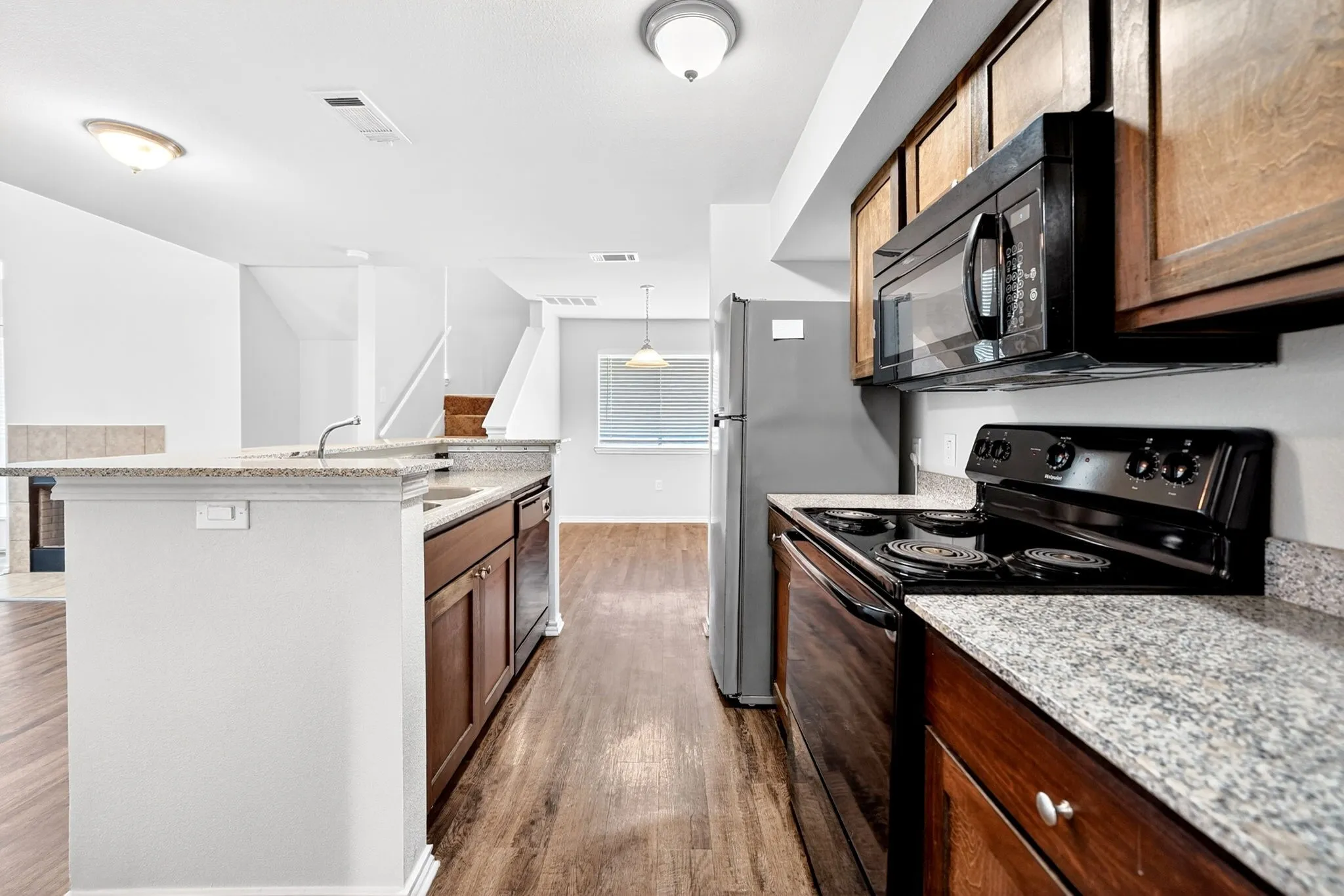 Kitchen featuring wood-finish flooring, granite-style countertops, stainless steel refrigerator, black electric range, and a black built-in microwave