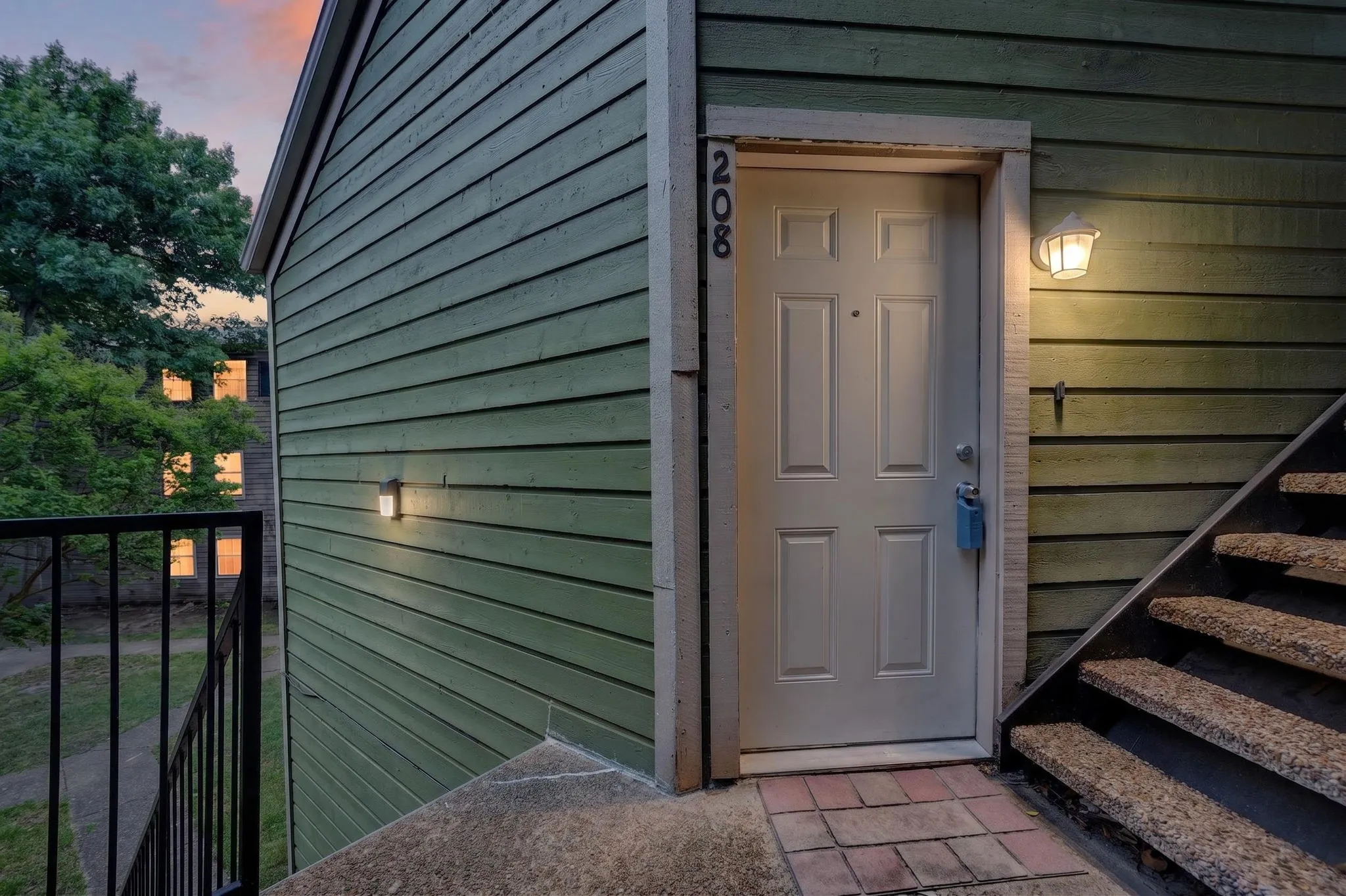 Exterior entrance featuring durable horizontal siding, a paneled entry door, exterior lighting fixtures, and a brick paver landing