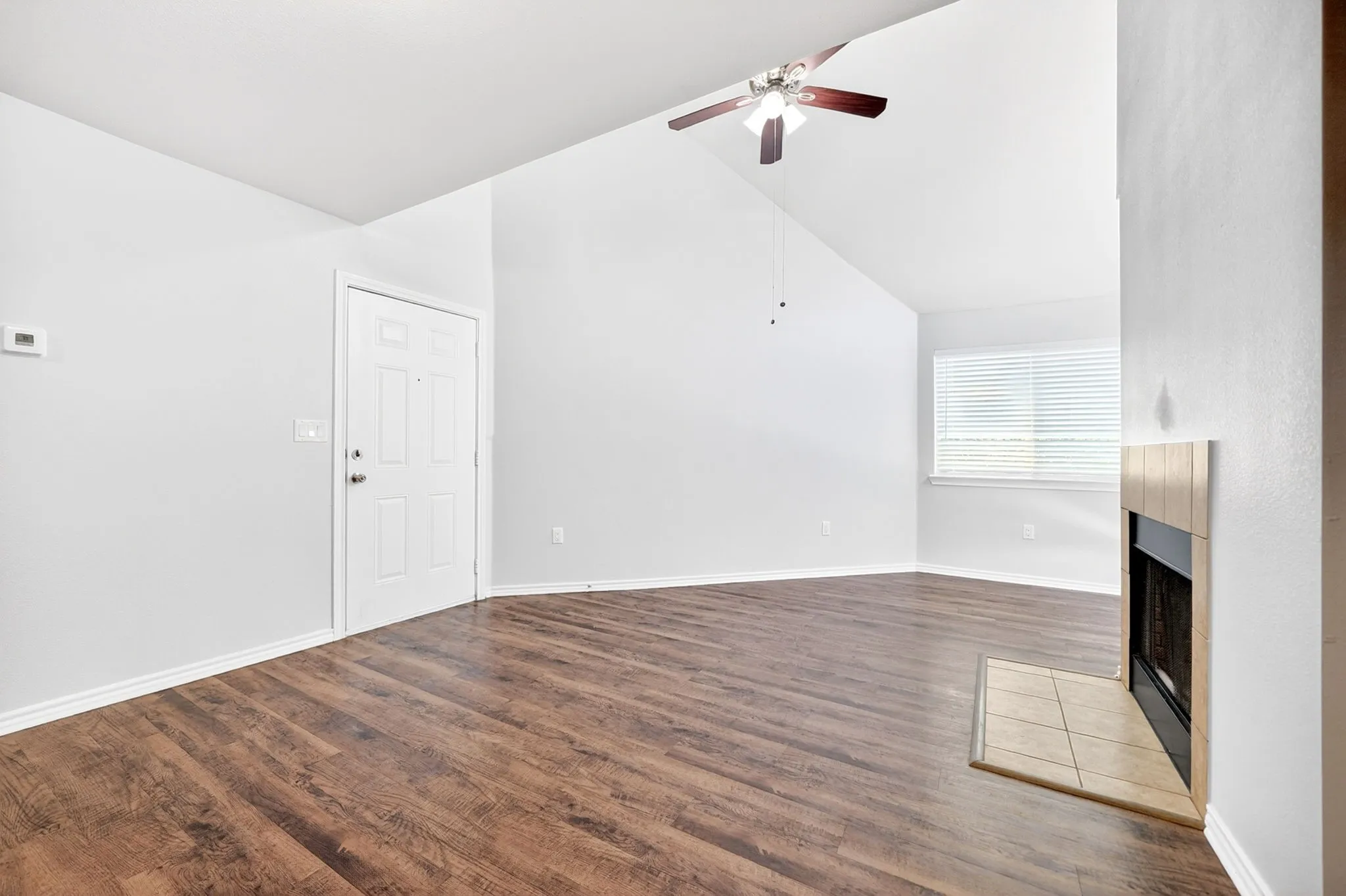 Spacious room featuring wood-finish flooring, a vaulted ceiling with a ceiling fan, and a fireplace with a tiled hearth and surround
