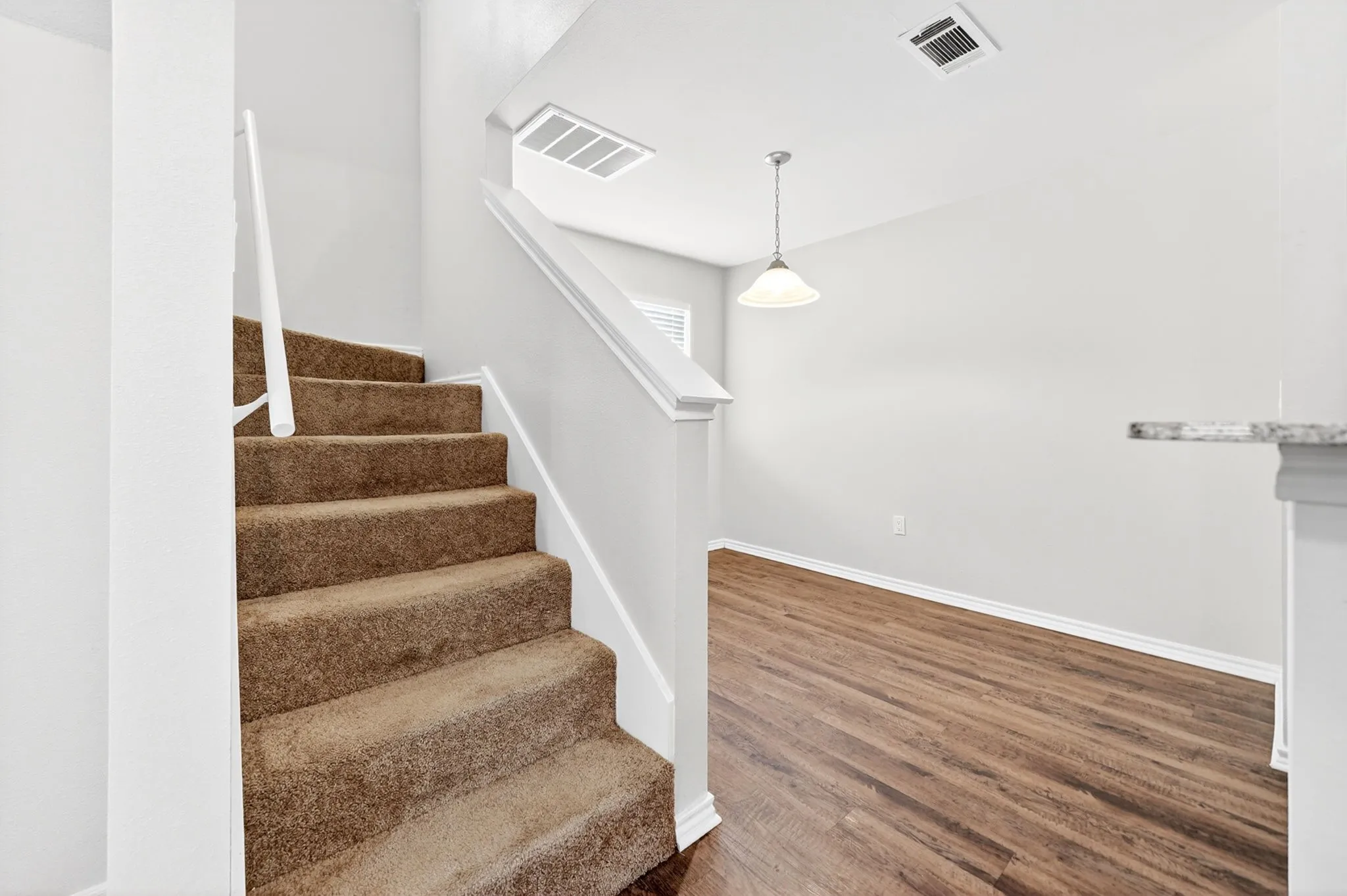 Carpeted staircase with white railings, featuring white walls, wood-finish flooring, and a ceiling-mounted pendant light fixture