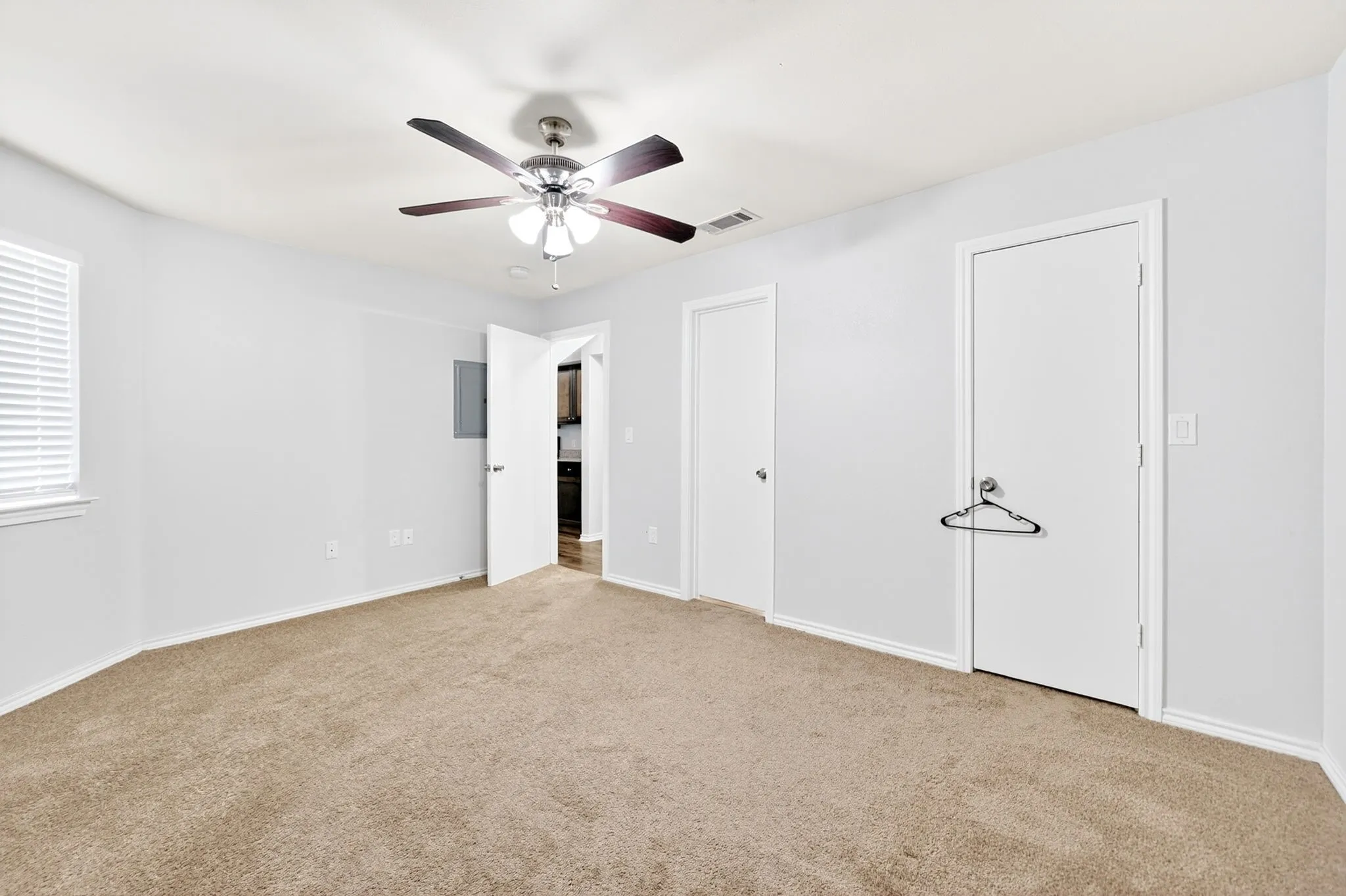Carpeted interior space featuring a ceiling fan with integrated lighting, white walls, and a window with horizontal blinds