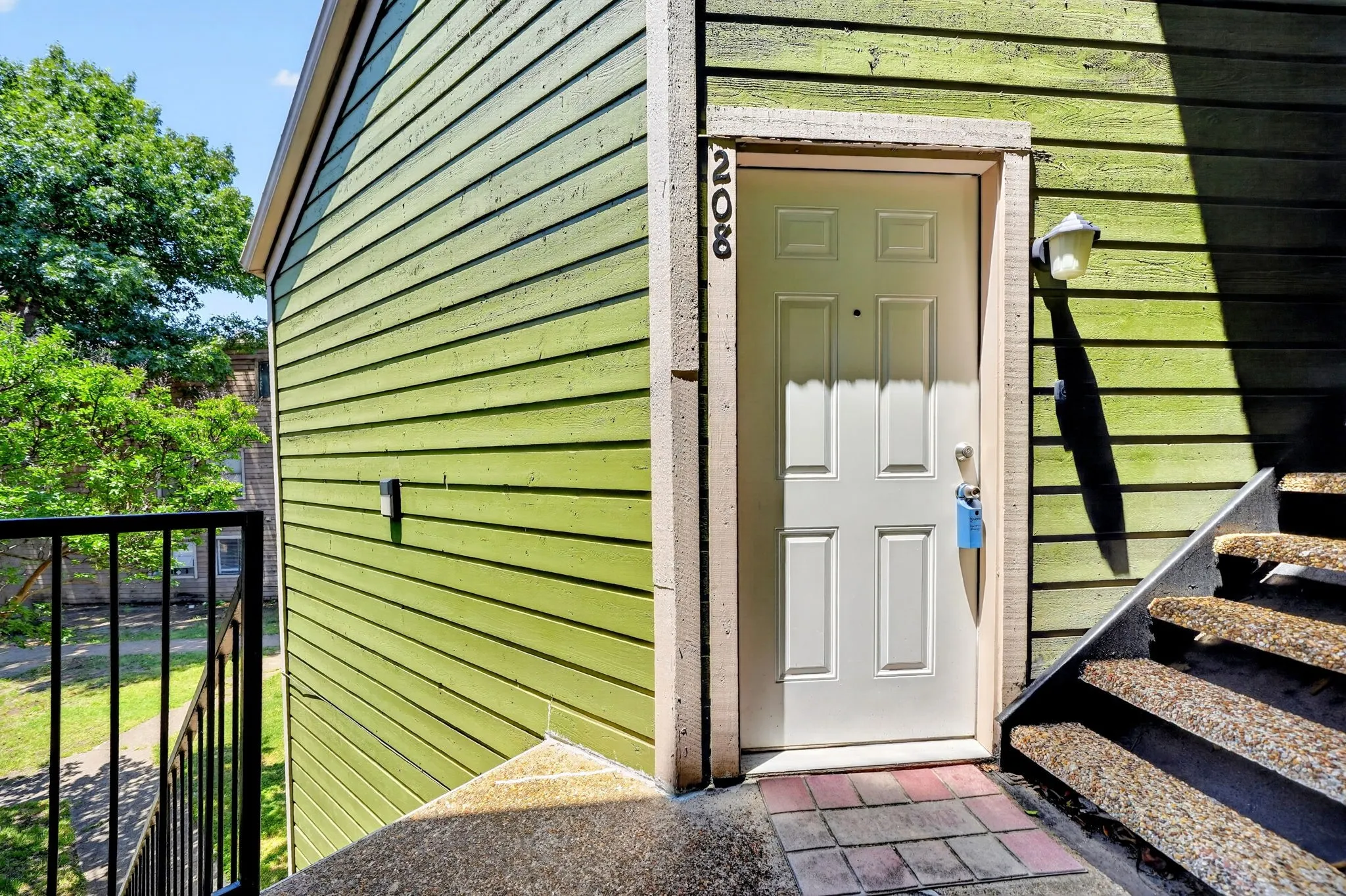 Entryway featuring a white paneled door with address numbering, exterior wall sconce, and green horizontal siding