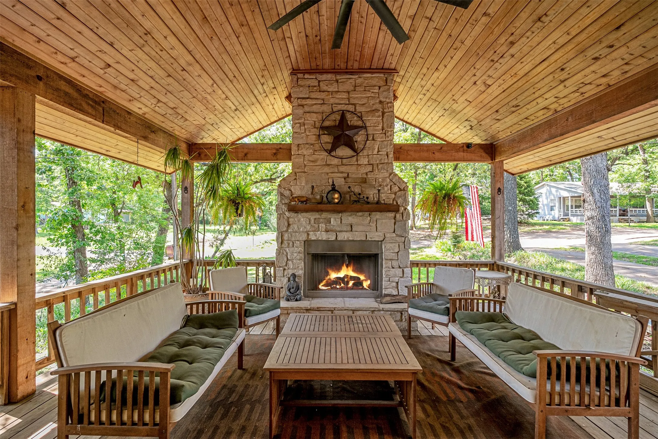 Expansive covered patio featuring a stone-clad fireplace, wood-planked ceiling, and wood-finish flooring