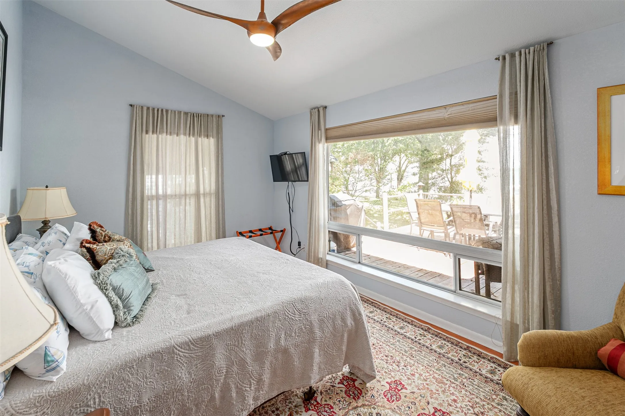 Vaulted ceiling bedroom with a contemporary ceiling fan, illuminated by a large picture window and an additional vertical window
