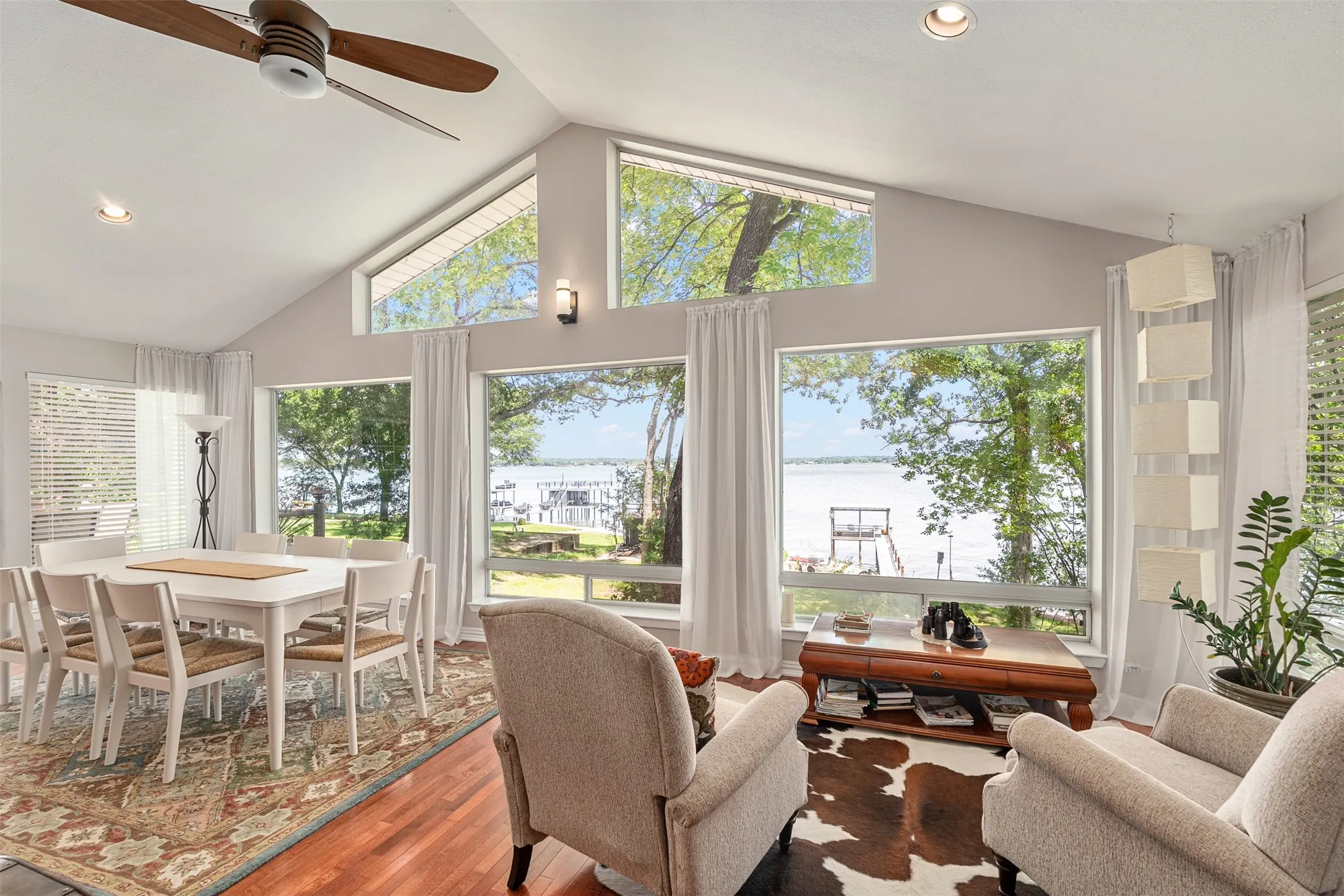 Vaulted ceiling living area featuring wood-finish flooring and expansive windows overlooking a body of water
