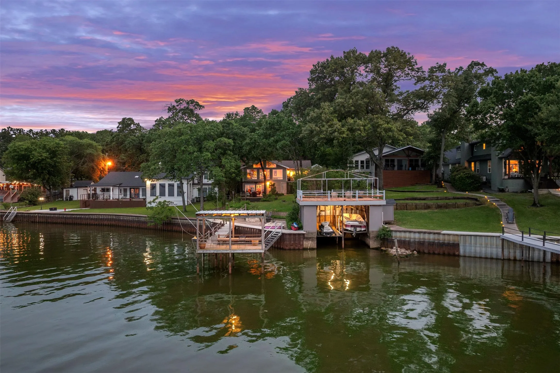 Waterfront property featuring multiple boat docks, a two-story boat house with upper deck, permanent seawall, and mature trees