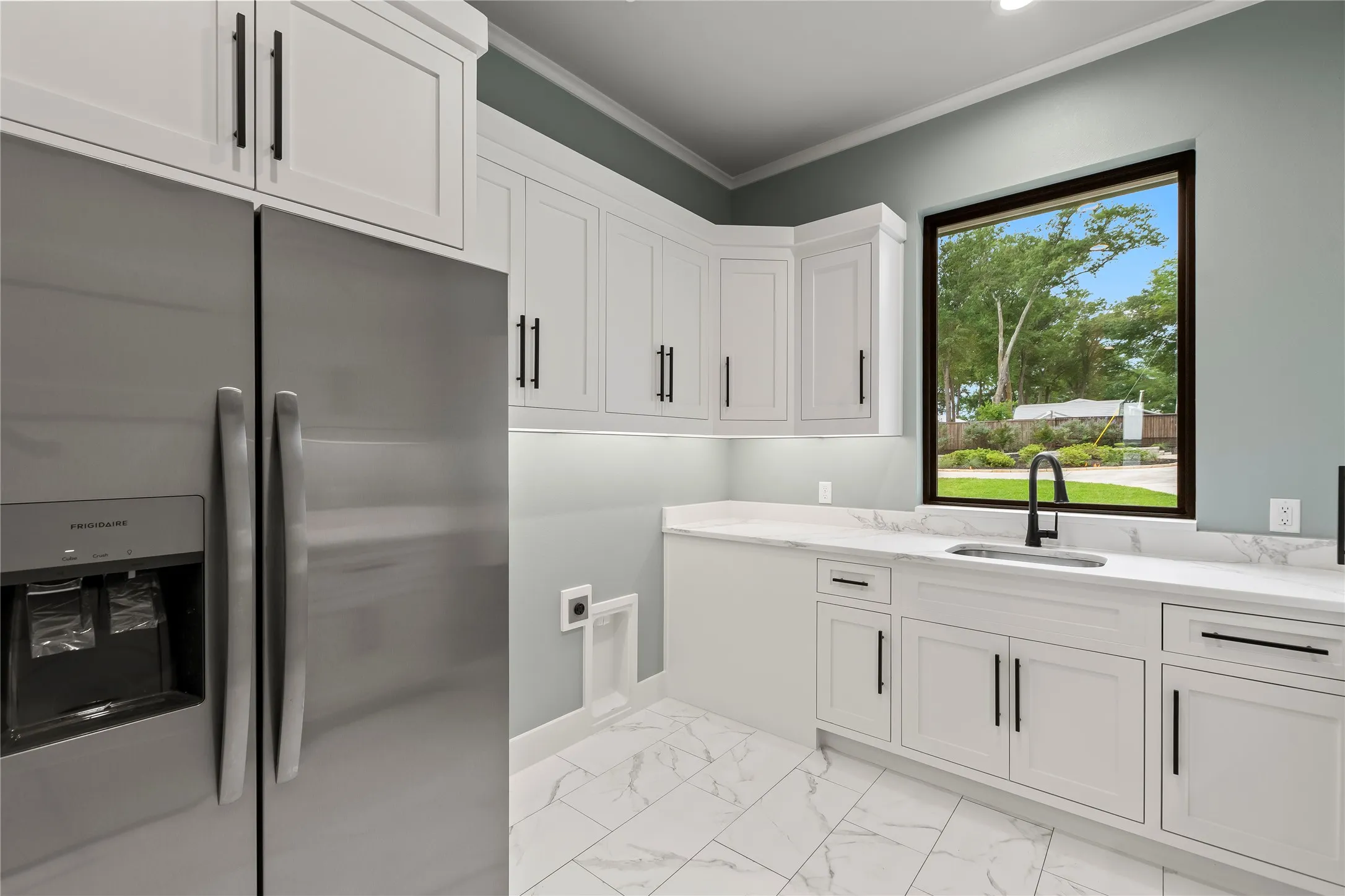 Functional oversized utility room complete with secondary fridge, large sink, and plentiful storage space.
