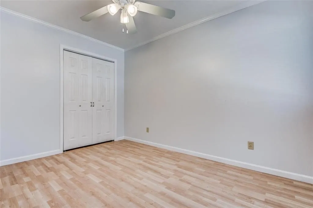 Bedroom featuring wood-finish flooring, light neutral walls, white crown molding, and a built-in closet with bi-fold doors