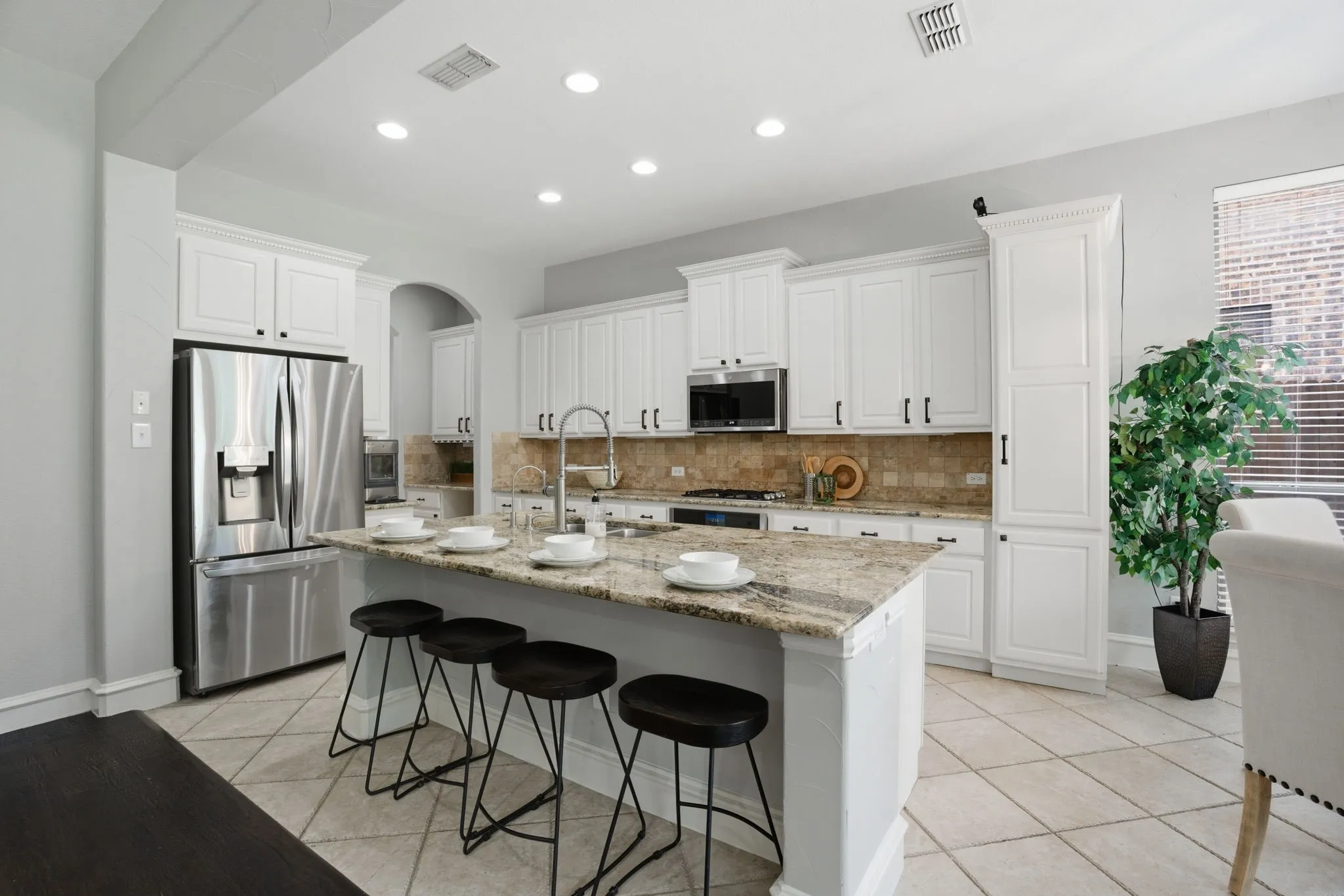 Well-appointed kitchen featuring an expansive center island with seating, stainless steel appliances, white cabinetry with dark hardware, a tile backsplash, and diagonal tile flooring