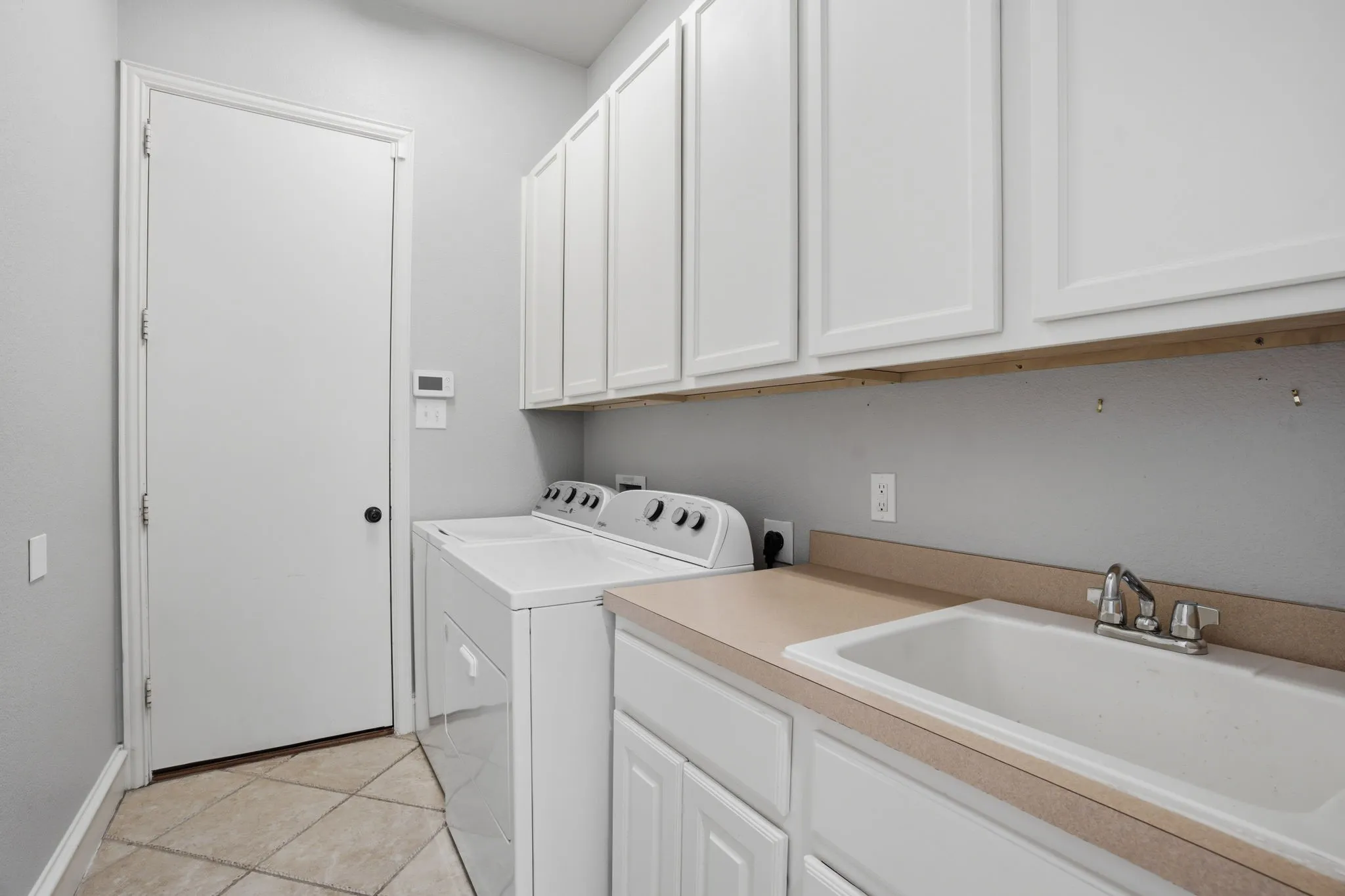 Dedicated laundry area featuring white shaker-style cabinetry, a utility sink with chrome faucet, and a light-toned countertop