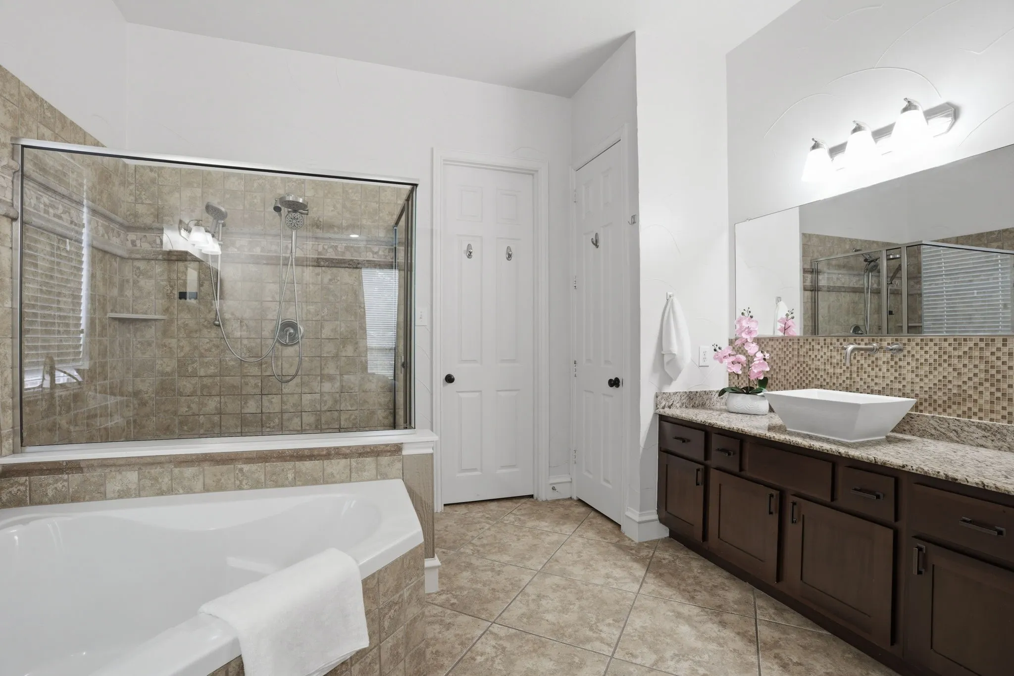 Bathroom featuring a glass-enclosed shower, a built-in soaking tub, a dark wood-finish vanity with a granite countertop, a vessel sink, and an extensive tiled backsplash