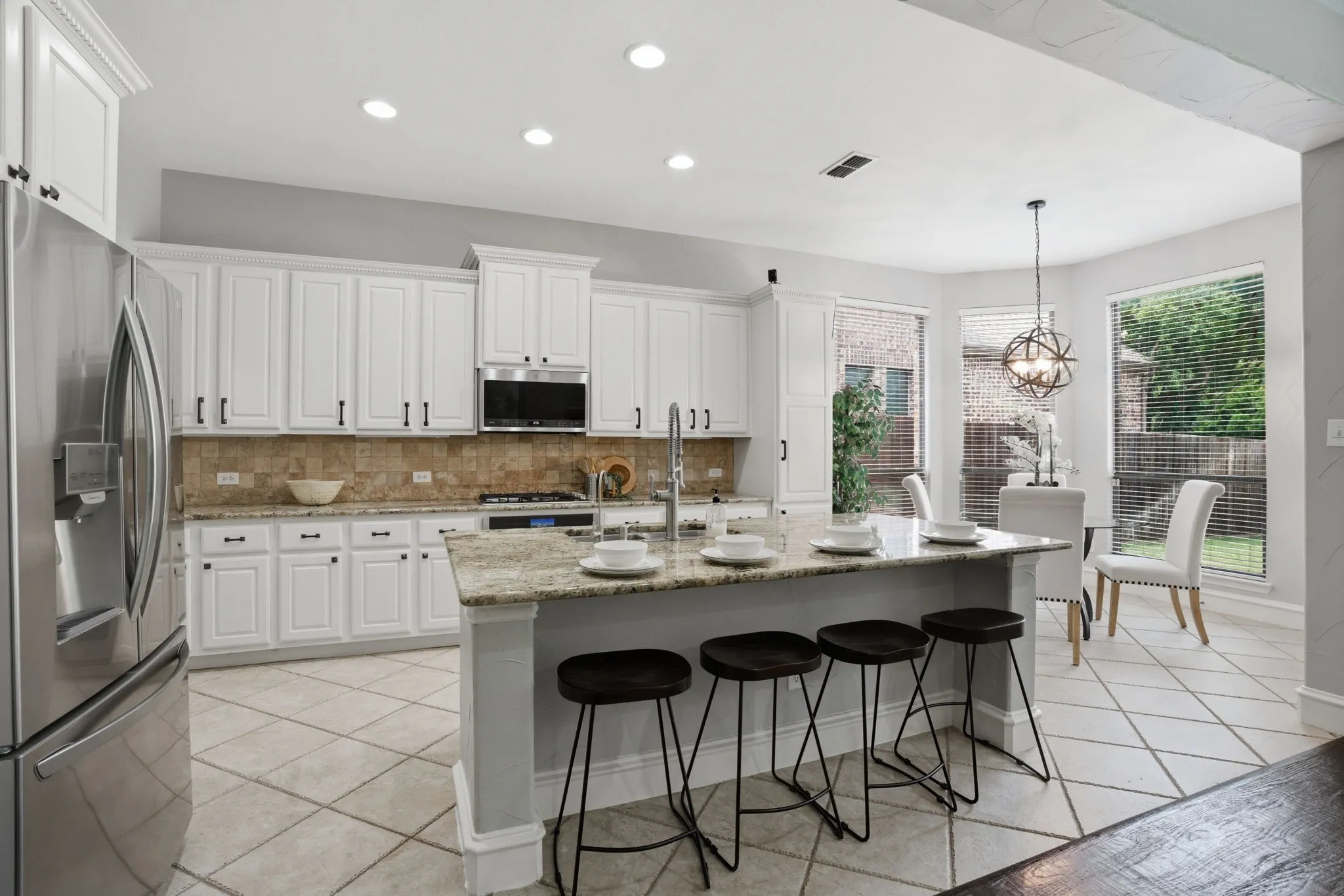 Bright kitchen featuring white cabinetry, a stone-tiled backsplash, and upgraded stainless steel appliances