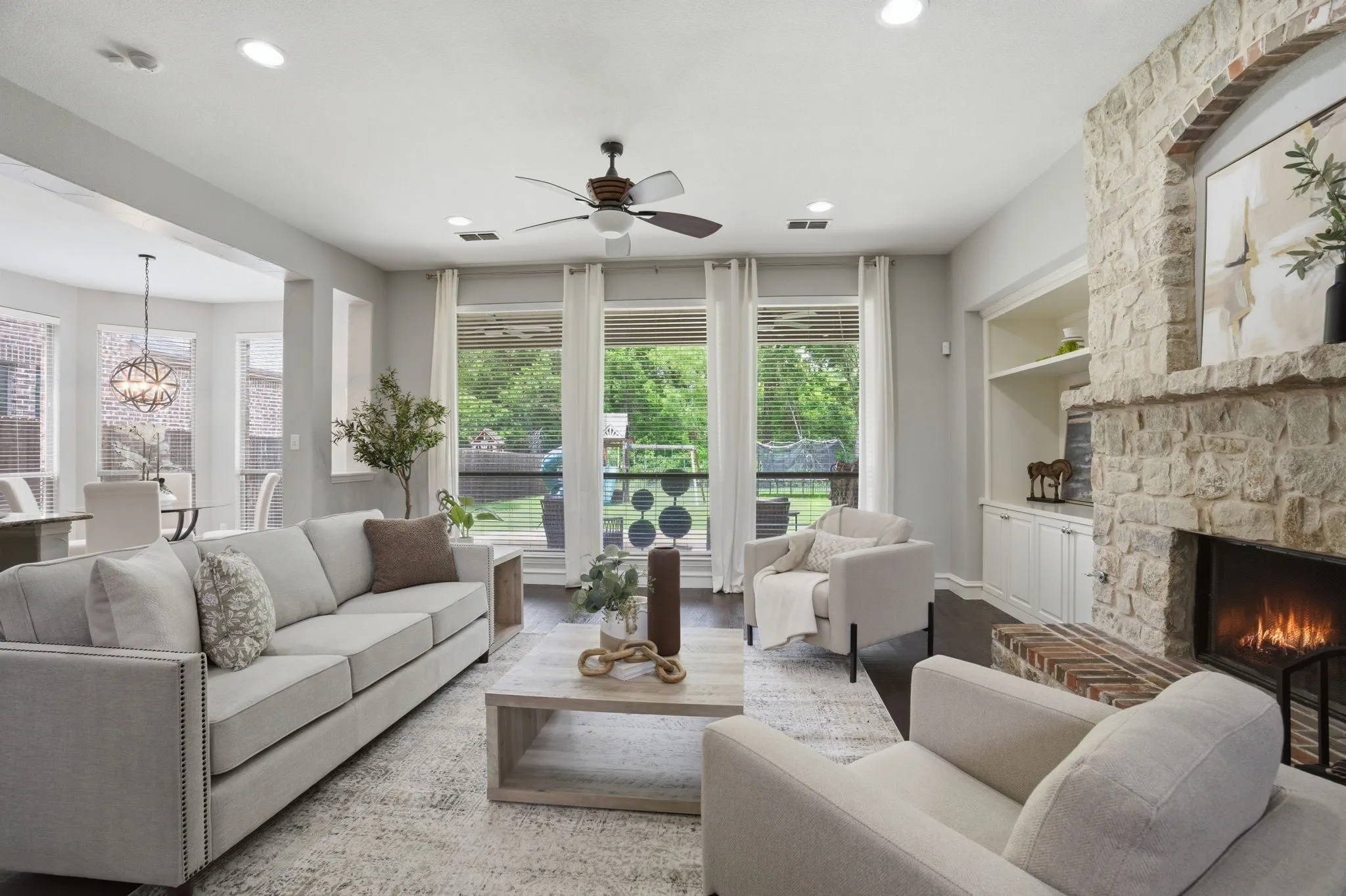 Spacious living area featuring a stone fireplace with a hearth, dark wood-finish flooring, recessed lighting, and a ceiling fan