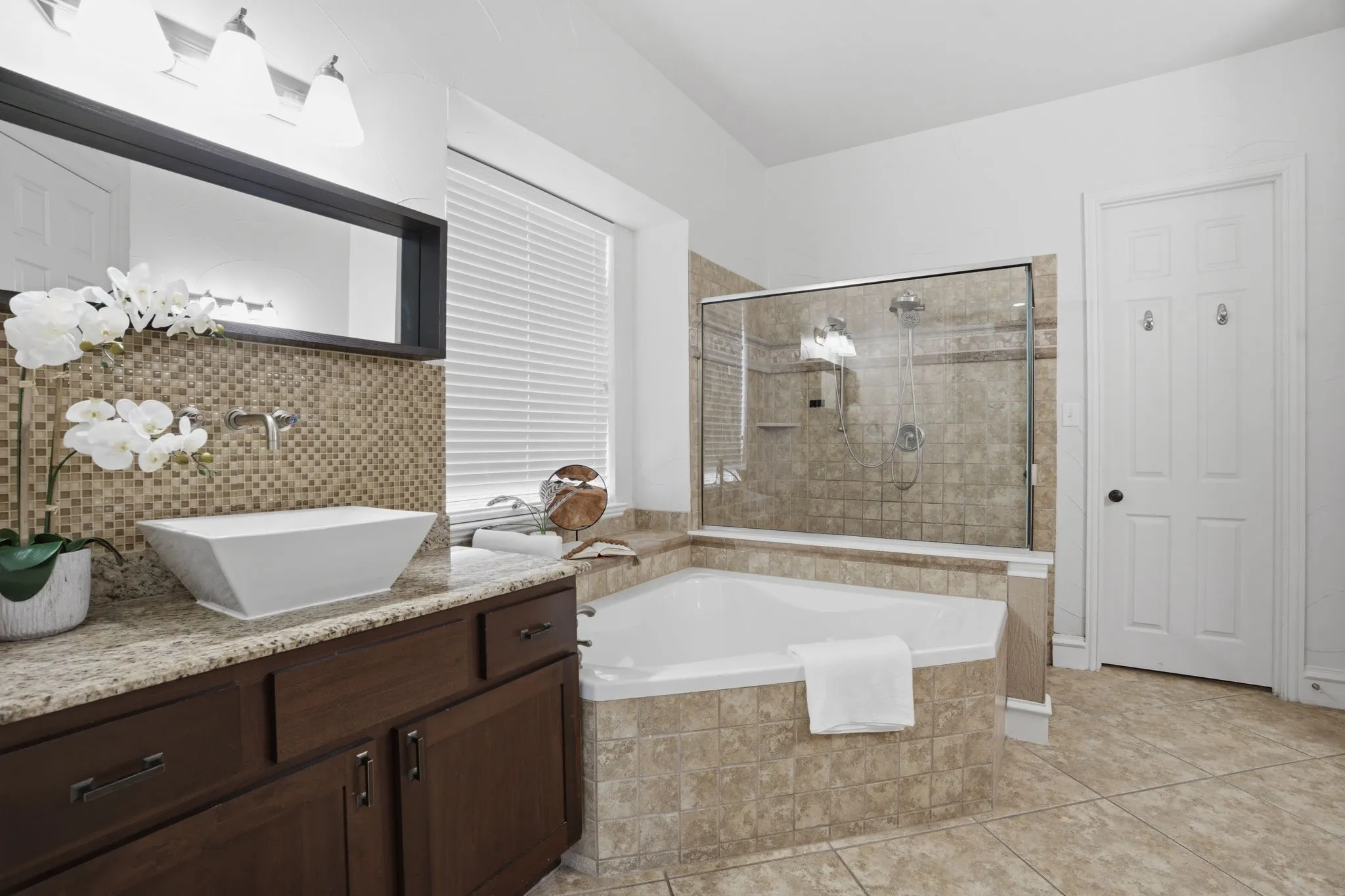 Bathroom featuring a corner soaking tub, a glass-enclosed shower, a vanity with a vessel sink, and a wall-mounted faucet