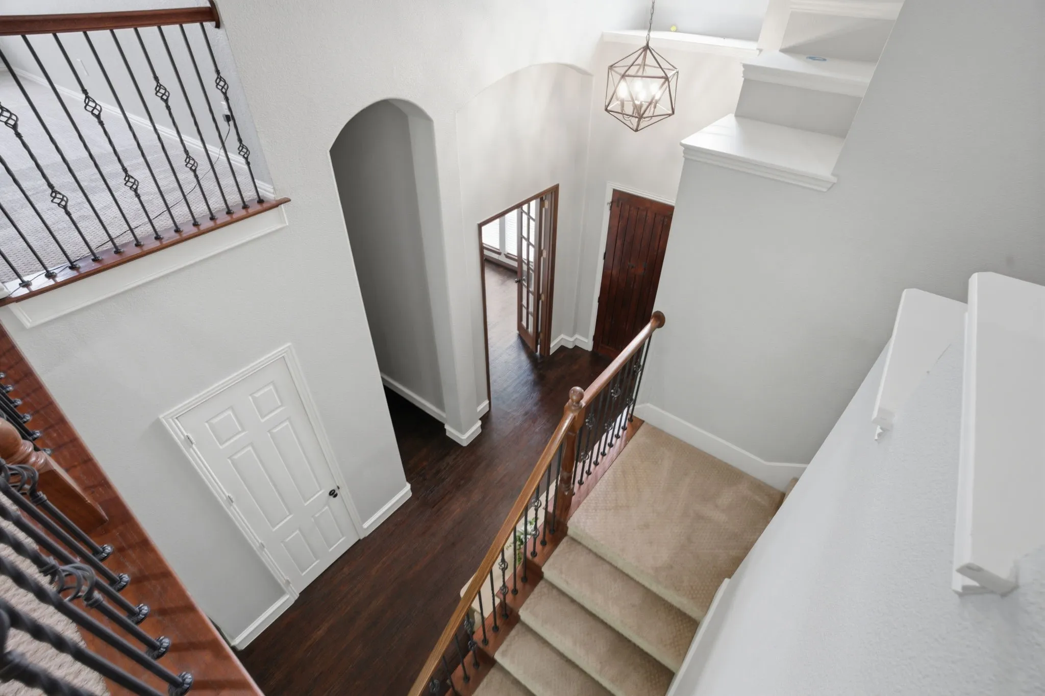 Two-story foyer featuring wood-finish flooring, a geometric pendant light fixture, and arched doorways