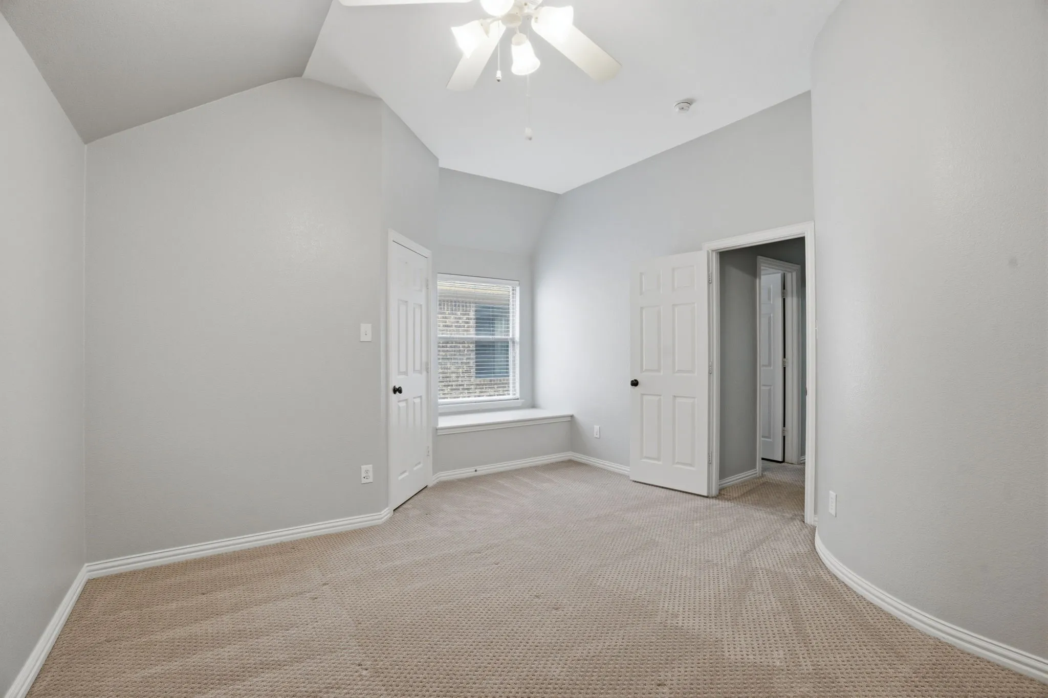 Carpeted room featuring a window seat, vaulted ceilings, and a ceiling fan