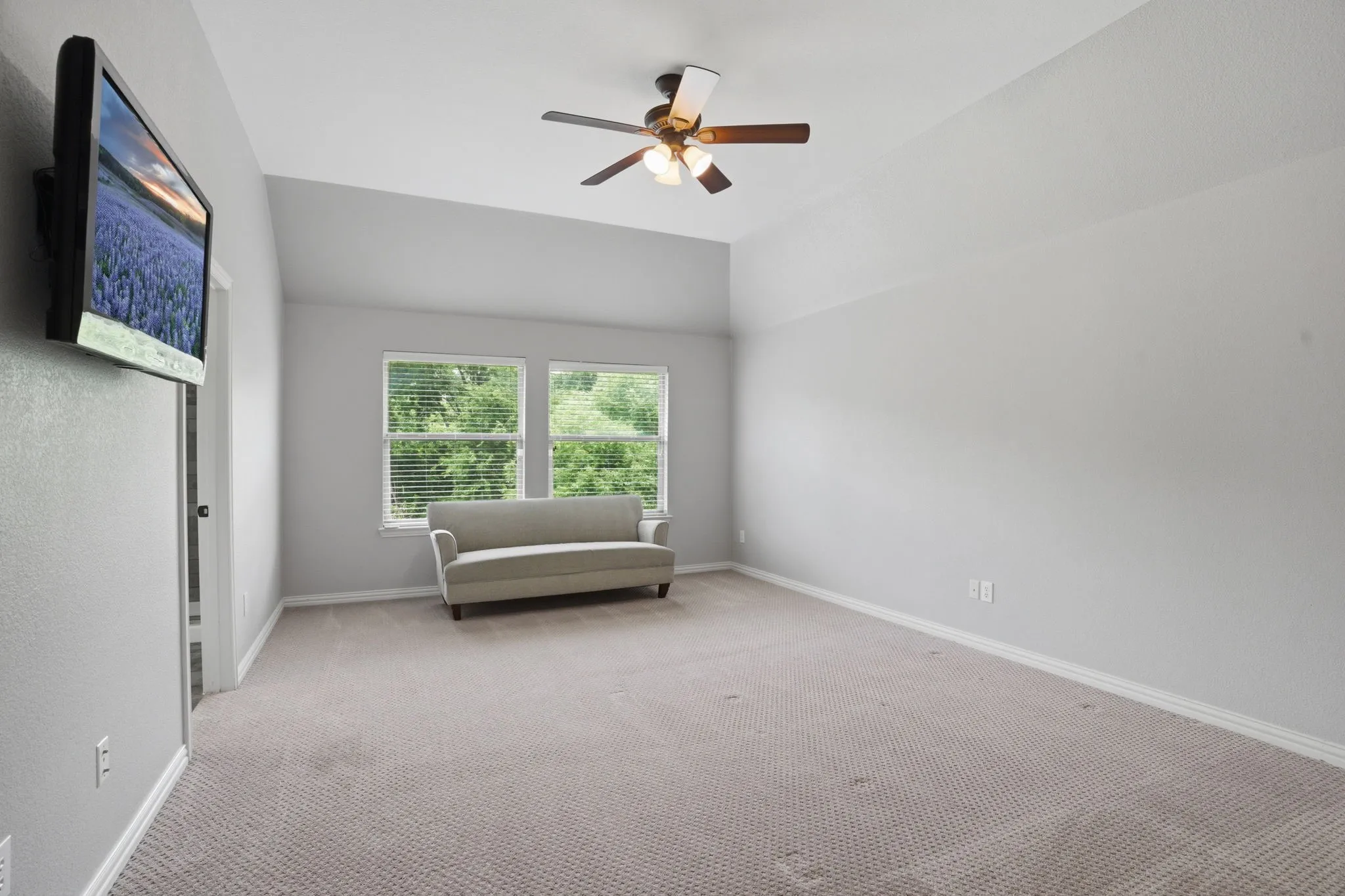 2nd floor primary bedroom featuring vaulted ceilings, a ceiling fan with light and fixture, two large windows with blinds, and neutral carpeting. Large walk in closet