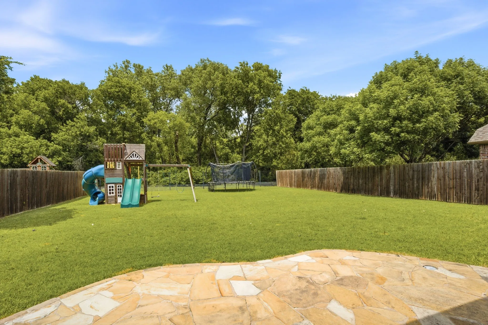 Expansive backyard featuring a stone patio, manicured lawn, and mature trees providing natural screening