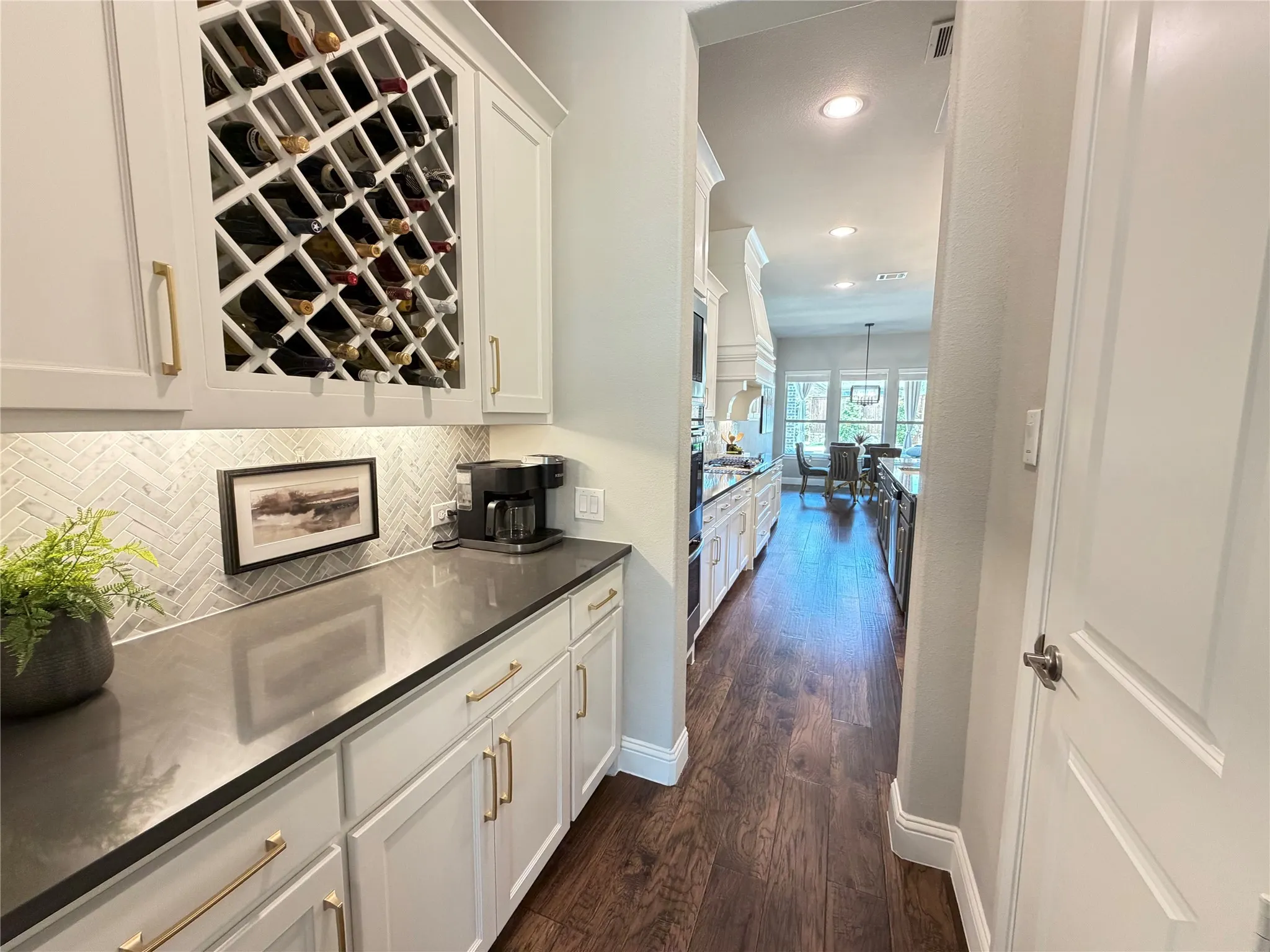 Custom butler's pantry with built-in wine storage, white cabinetry, dark countertop, and herringbone tile backsplash