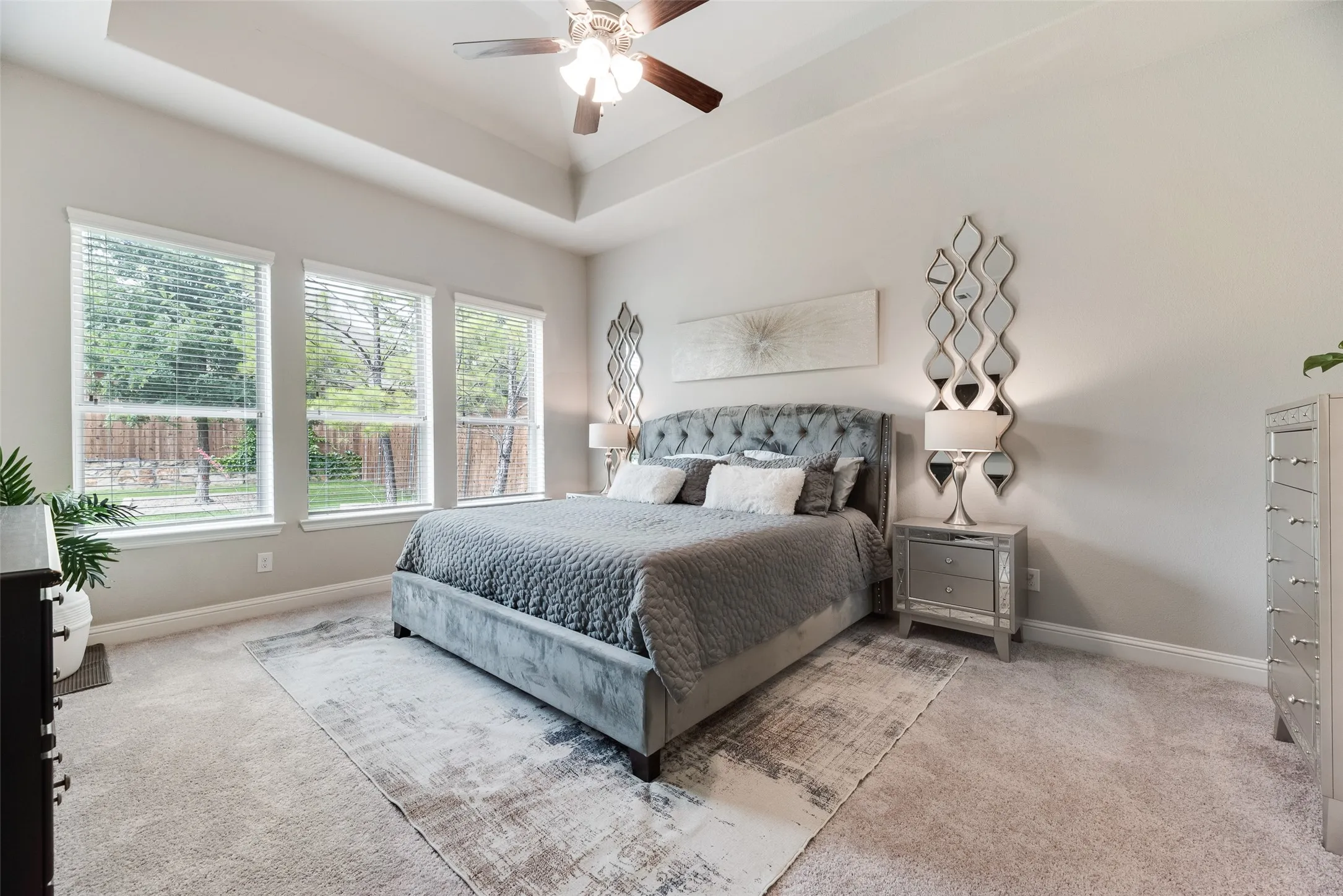 Room featuring a tray ceiling with a ceiling fan, three windows with blinds, and light-toned wall-to-wall carpeting
