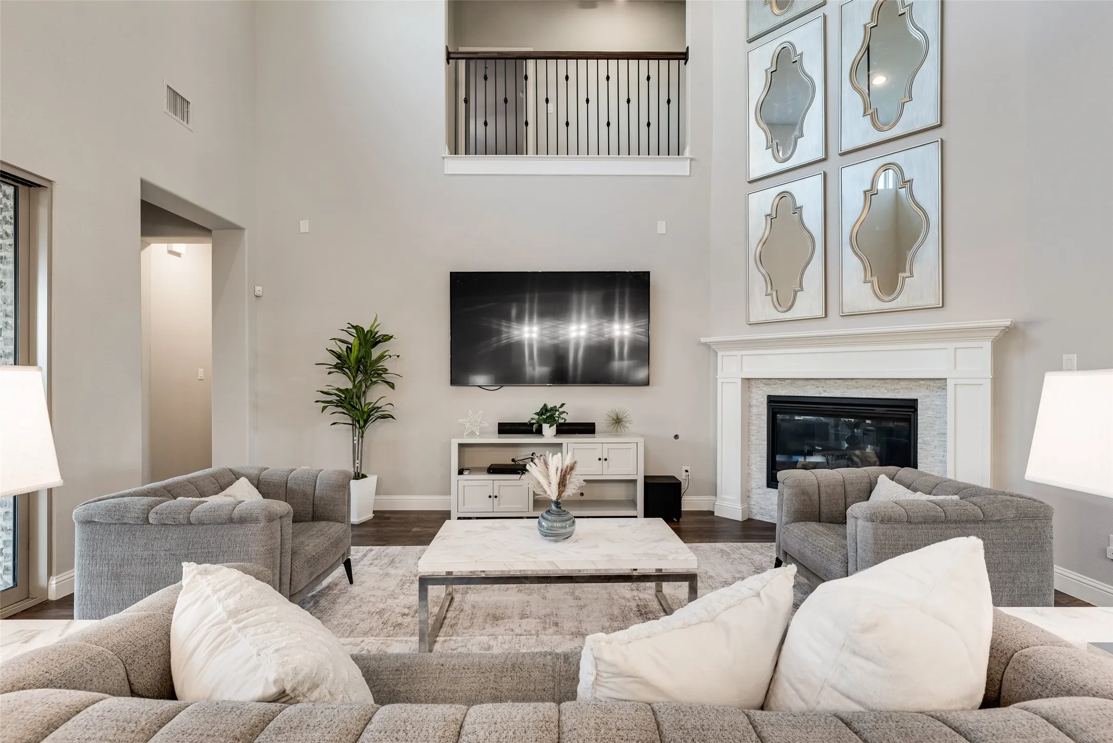 Living area featuring a soaring ceiling, a second-story interior balcony with iron balusters, a built-in fireplace with a stone surround and white mantel, hardwood flooring, and neutral wall tones