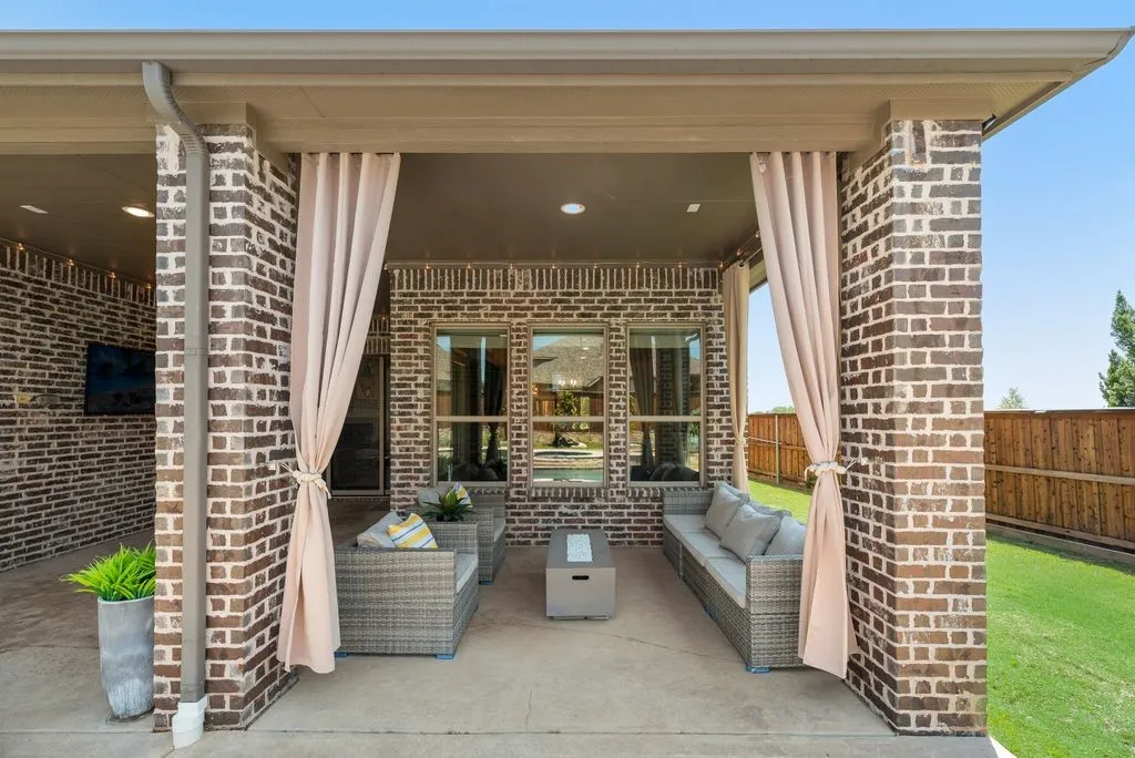 Covered outdoor patio featuring brick pillars, privacy drapes, and an outdoor television